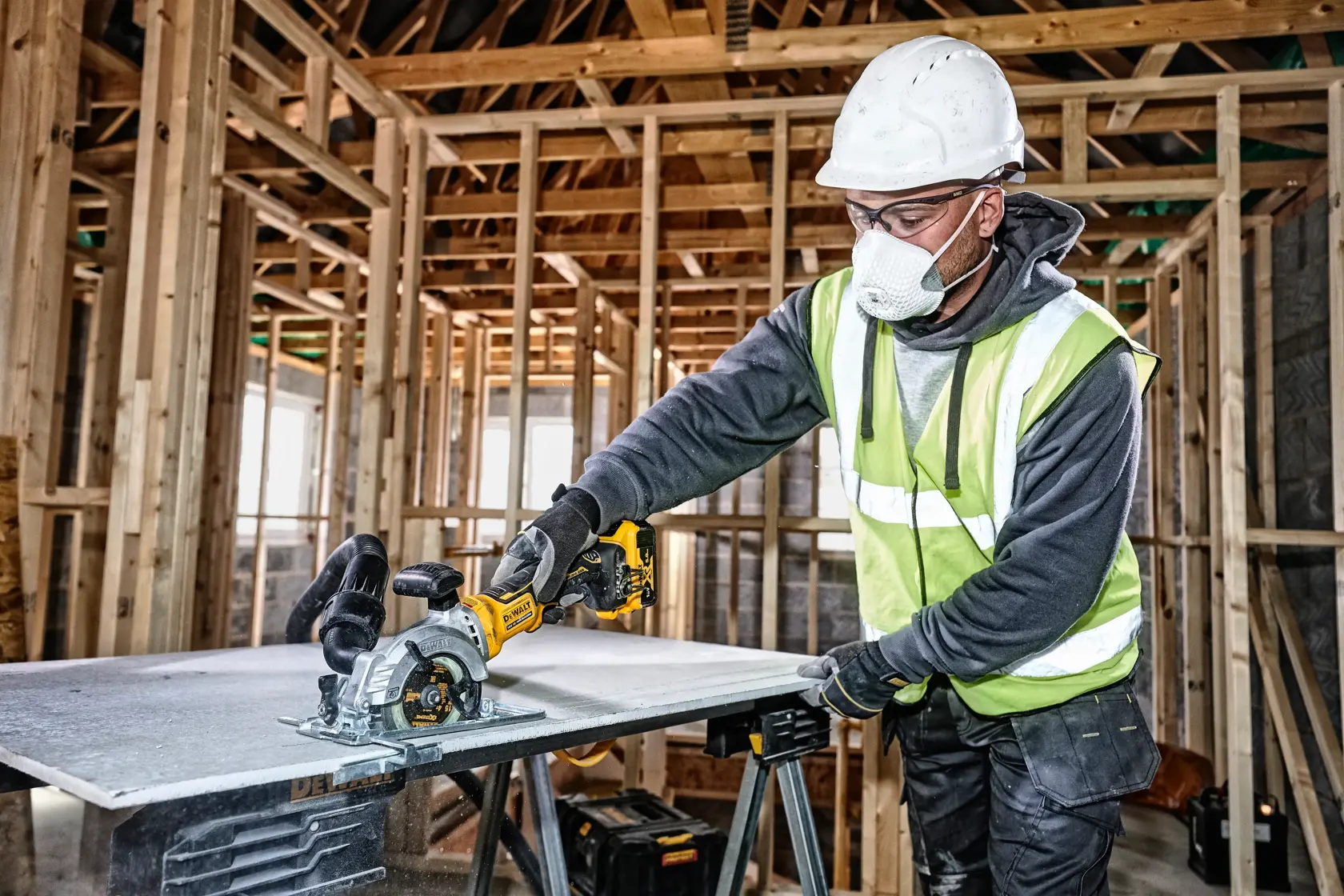 Worker uses a DEWALT cordless circular saw to cut a board at a construction site with wooden framing.