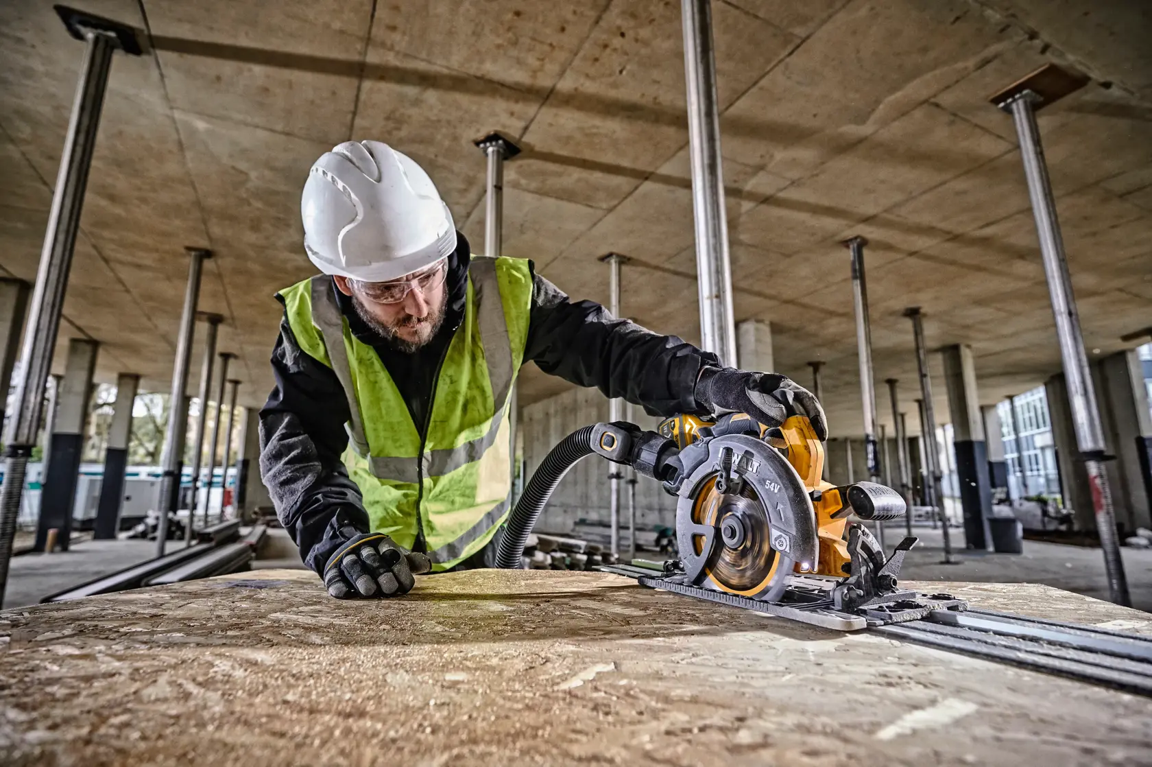 Worker uses a DEWALT circular saw to cut wood indoors, wearing safety gear and a reflective vest.