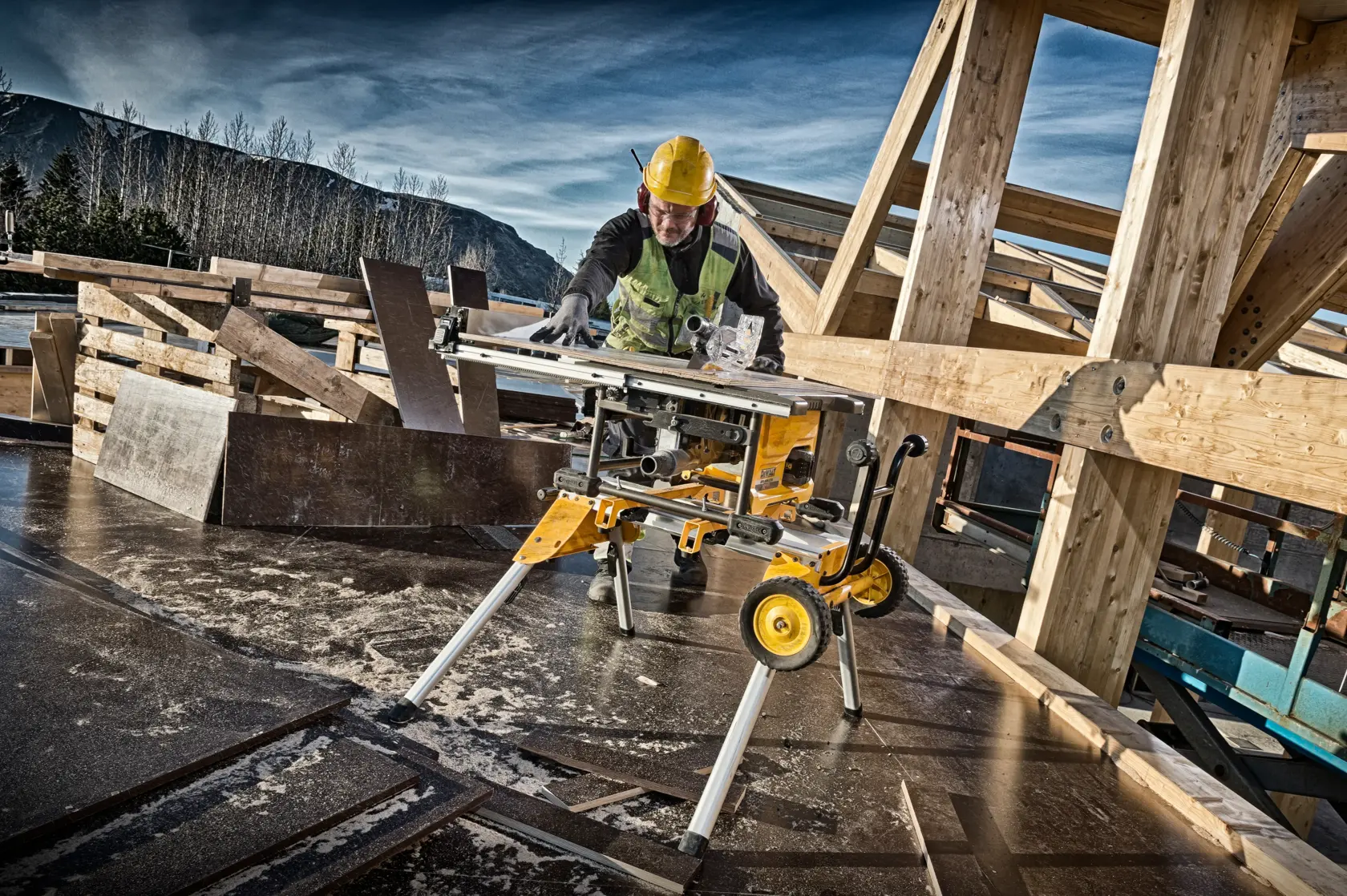 Arbeiter nutzt DEWALT DCS7485N Tischsäge auf Baustelle mit Holzbalken und Sicherheitsausrüstung.