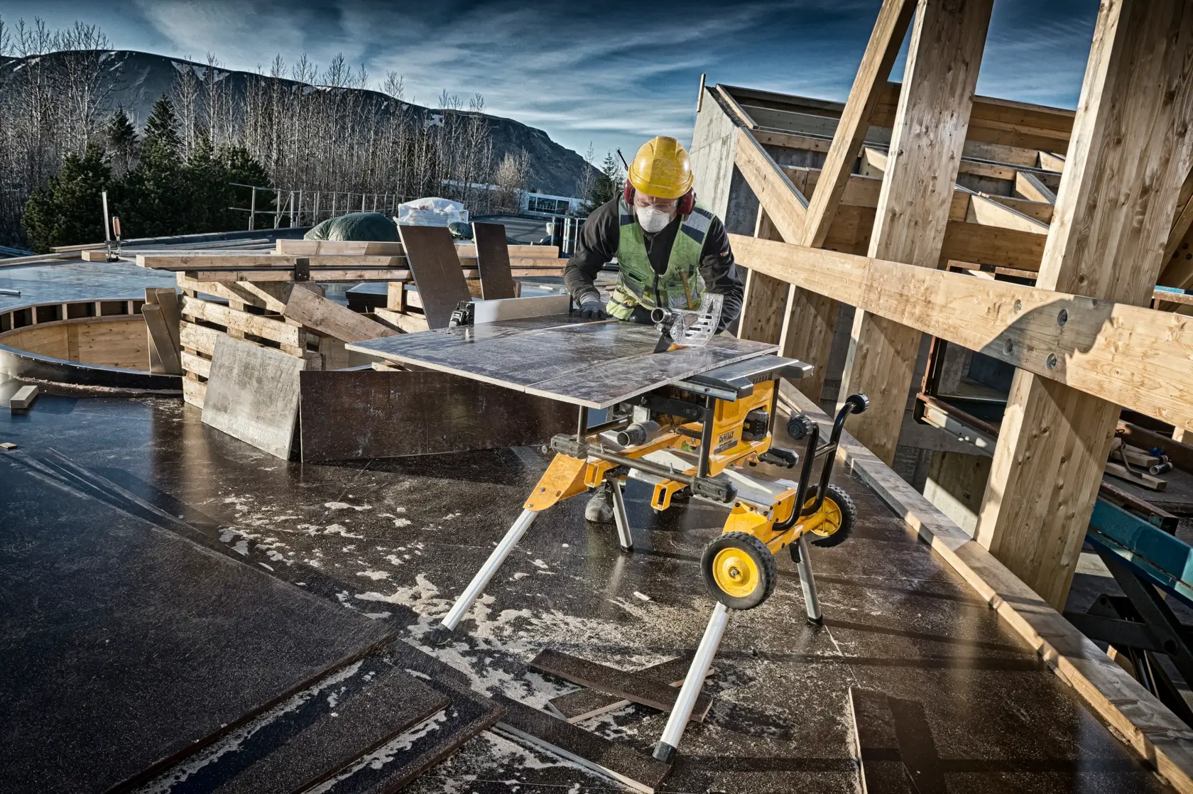 DEWALT DCS7485N Tischsäge auf Baustelle, Arbeiter mit Schutzausrüstung schneidet Holzplatten.