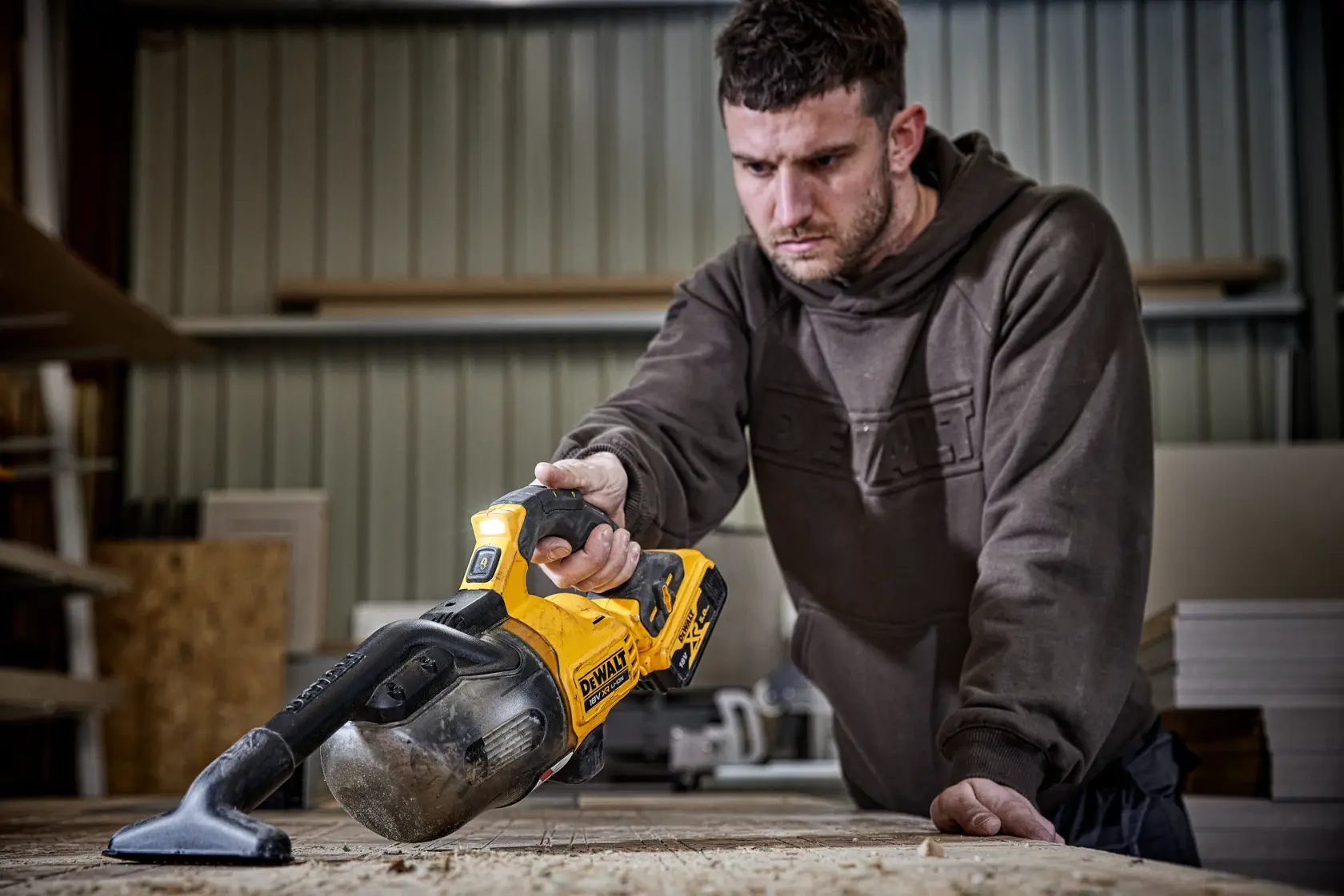 Persona usando aspiradora inalámbrica DEWALT DCV501LN para limpiar banco de madera en taller.