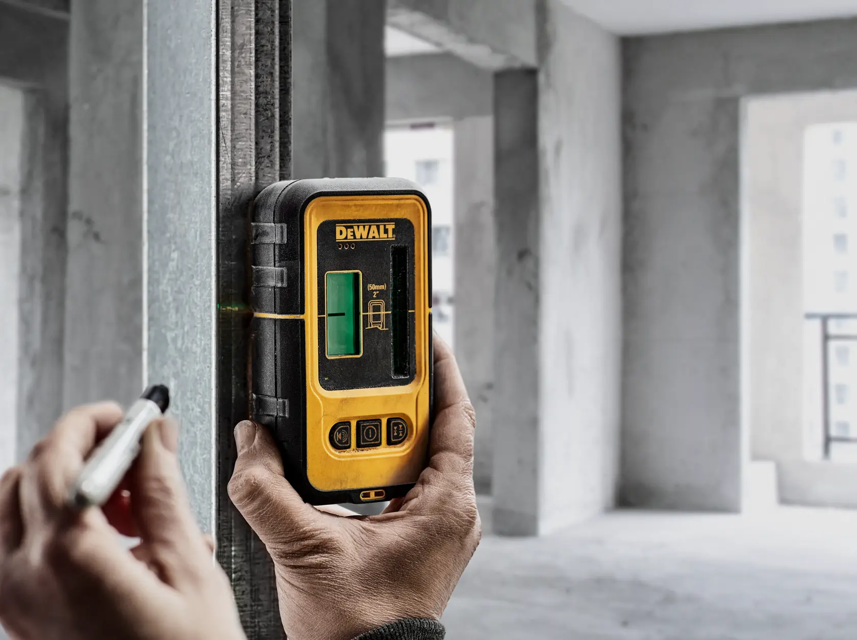 Persona utiliza detector láser DEWALT DE0892G en viga metálica dentro de edificio sin terminar.
