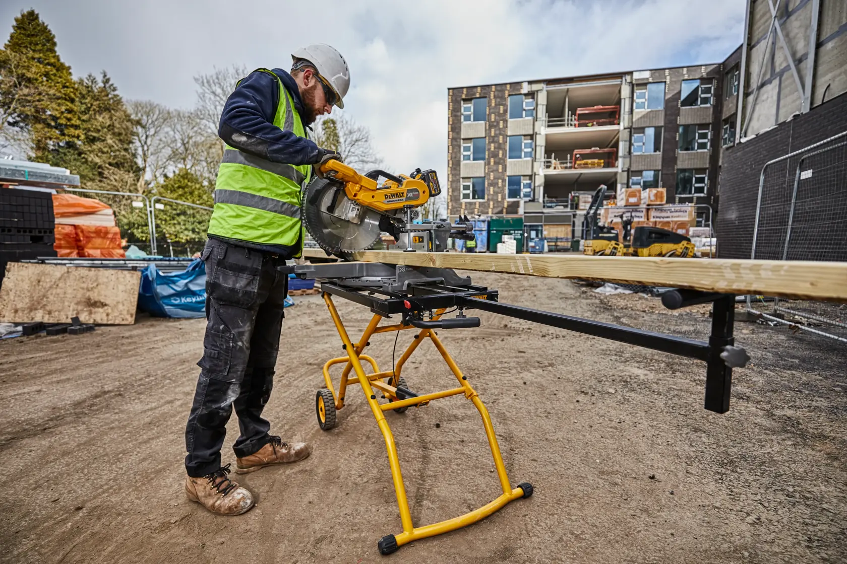 Trabajador usa soporte de sierra DEWALT DE7260 para cortar madera en obra. Edificio de fondo.