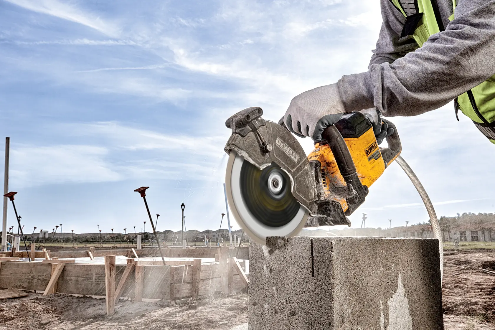 Persona corta bloque de hormigón al aire libre con una sierra DEWALT; polvo visible.