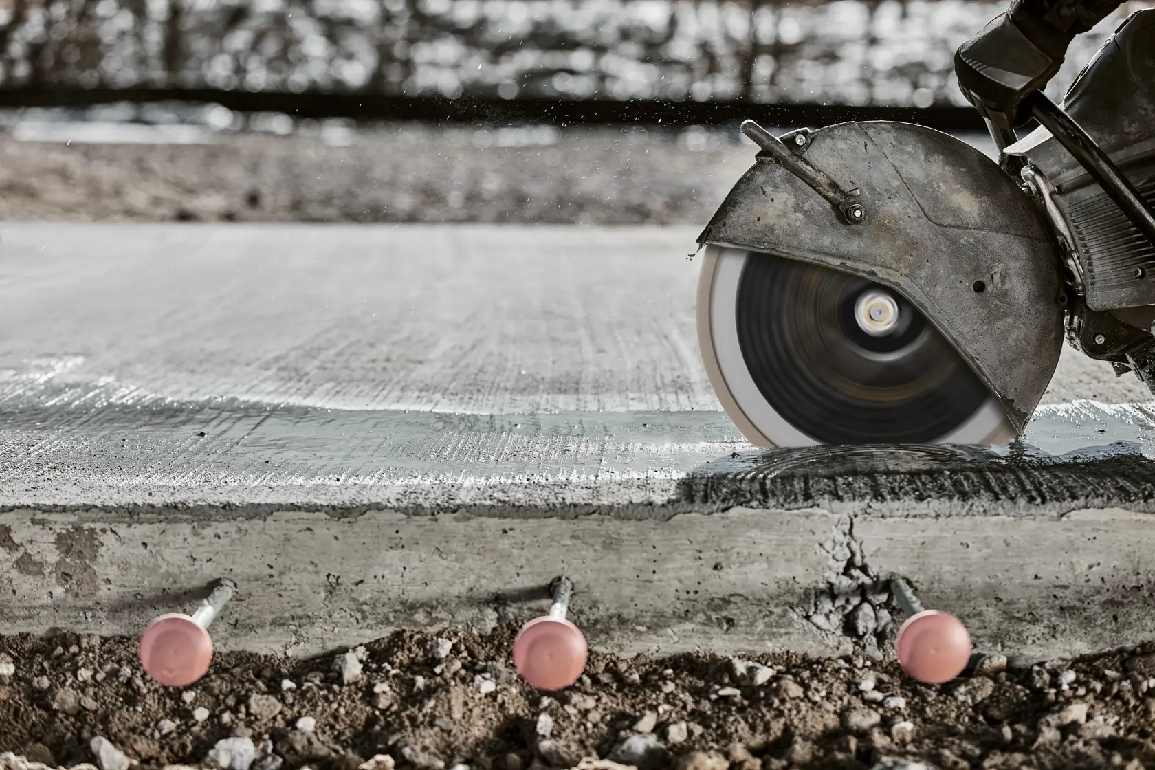 Circular saw cutting through concrete slab, with bolts visible underneath.