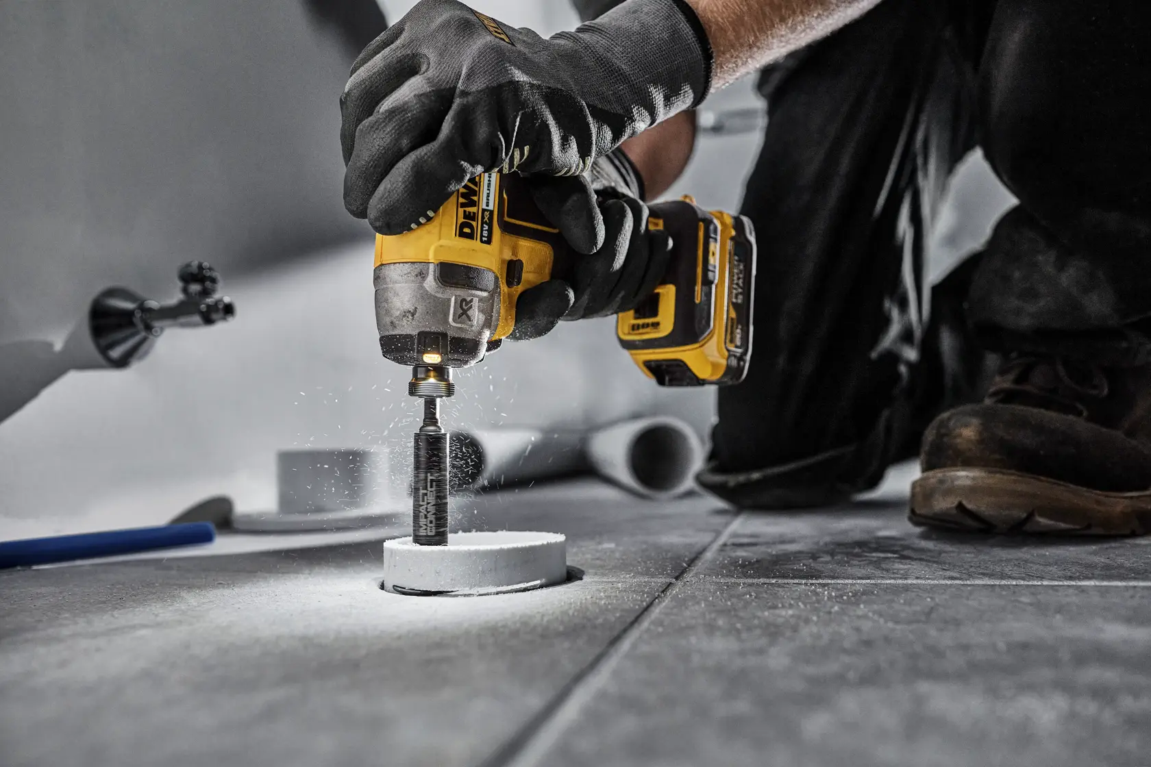 Persona usa taladro DEWALT con DT20563 para cortar baldosa en el suelo. Utiliza guantes de seguridad.