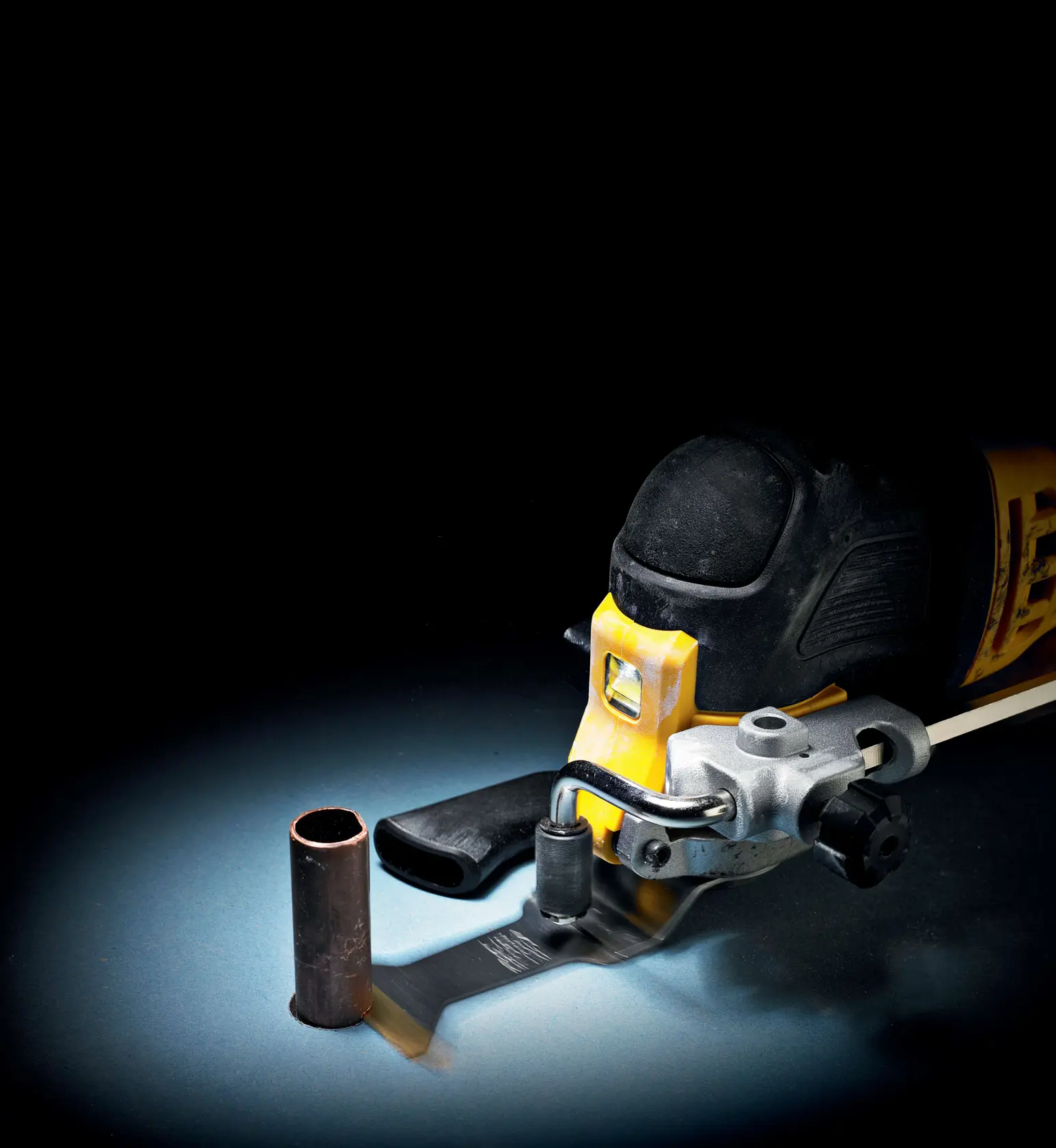 DEWALT Oszillationswerkzeug schneidet ein Metallrohr vor dunklem Hintergrund.
