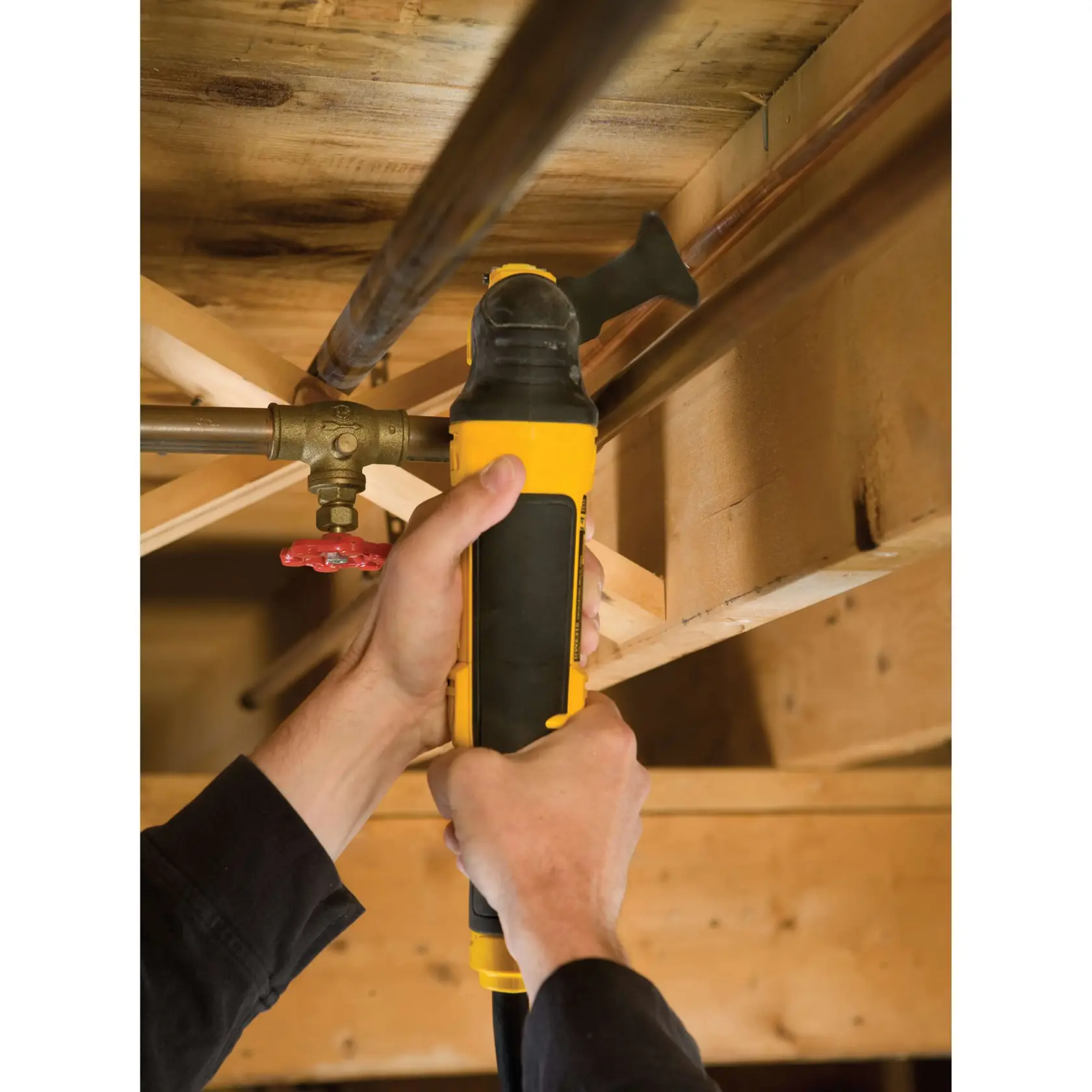 Hände schneiden mit einem DEWALT Werkzeug ein Metallrohr unter einer Holzdecke.