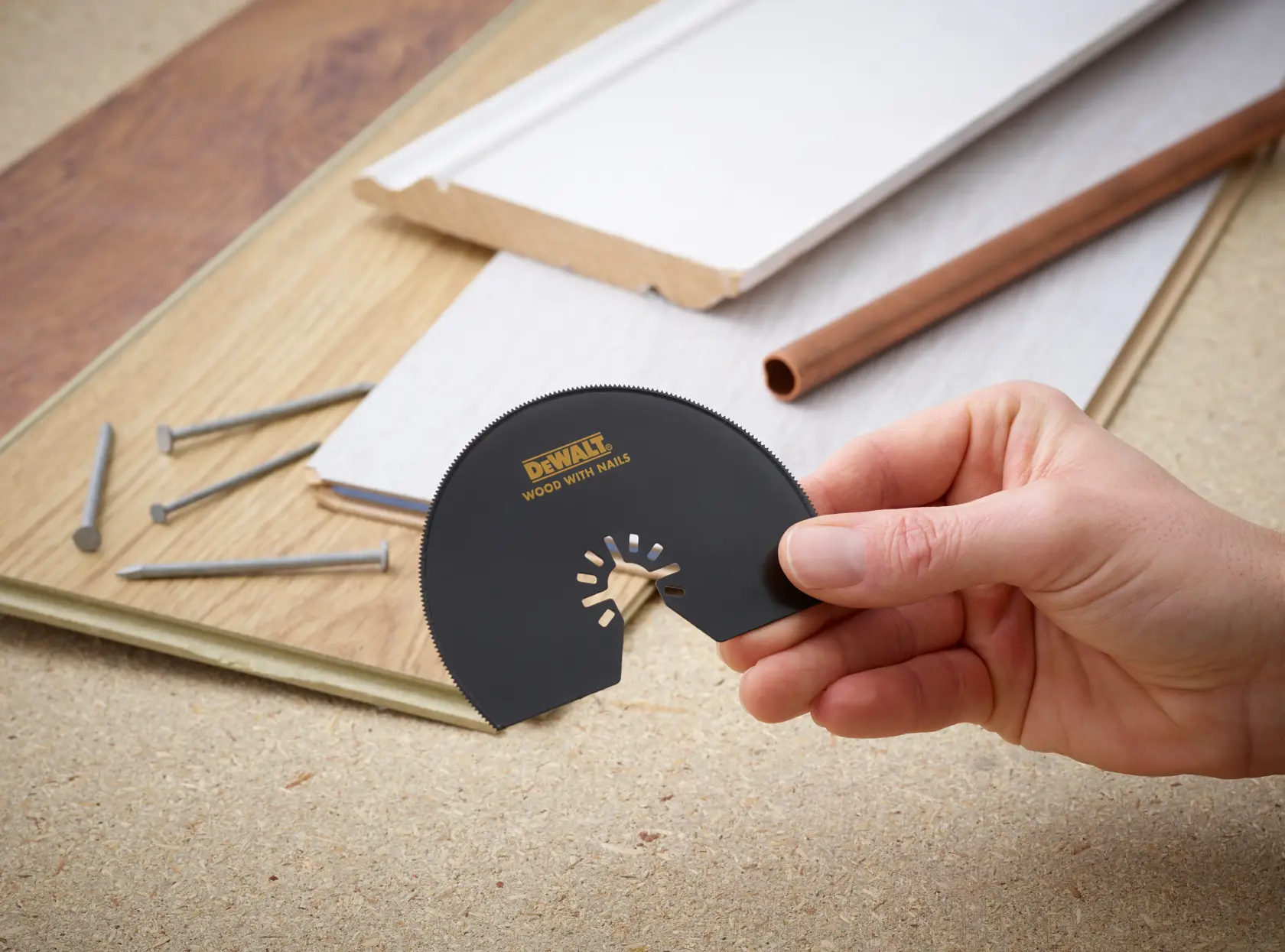 Hand hält DEWALT DT20708 Sägeblatt, mit Holz, Nägeln und Rohr im Hintergrund.
