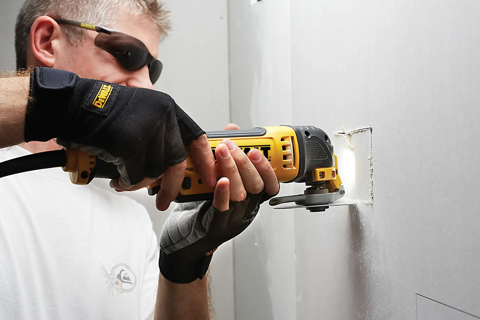 Person schneidet mit einem DEWALT Oszillationswerkzeug ein rechteckiges Loch in eine Trockenbauwand.