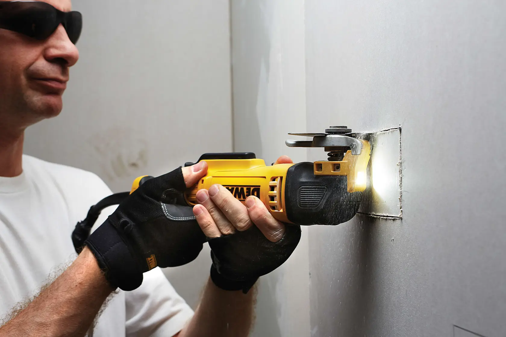 Person schneidet mit einem DEWALT Multitool und Handschuhen ein Quadrat in Trockenbauwand.