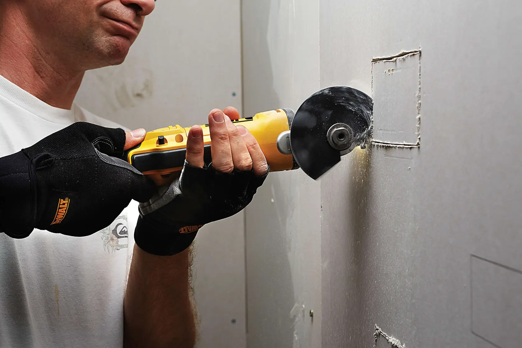 Person schneidet mit DEWALT Werkzeug und Handschuhen eine quadratische Öffnung in eine Trockenbauwand.