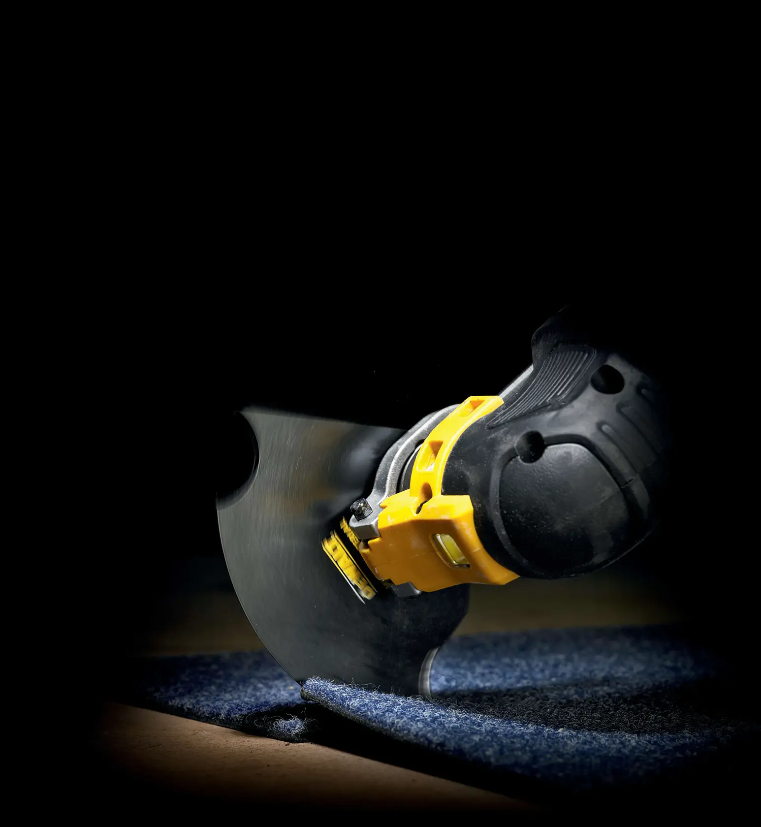 DEWALT Werkzeug schneidet Teppich mit Rundklinge, Nahaufnahme vor dunklem Hintergrund.