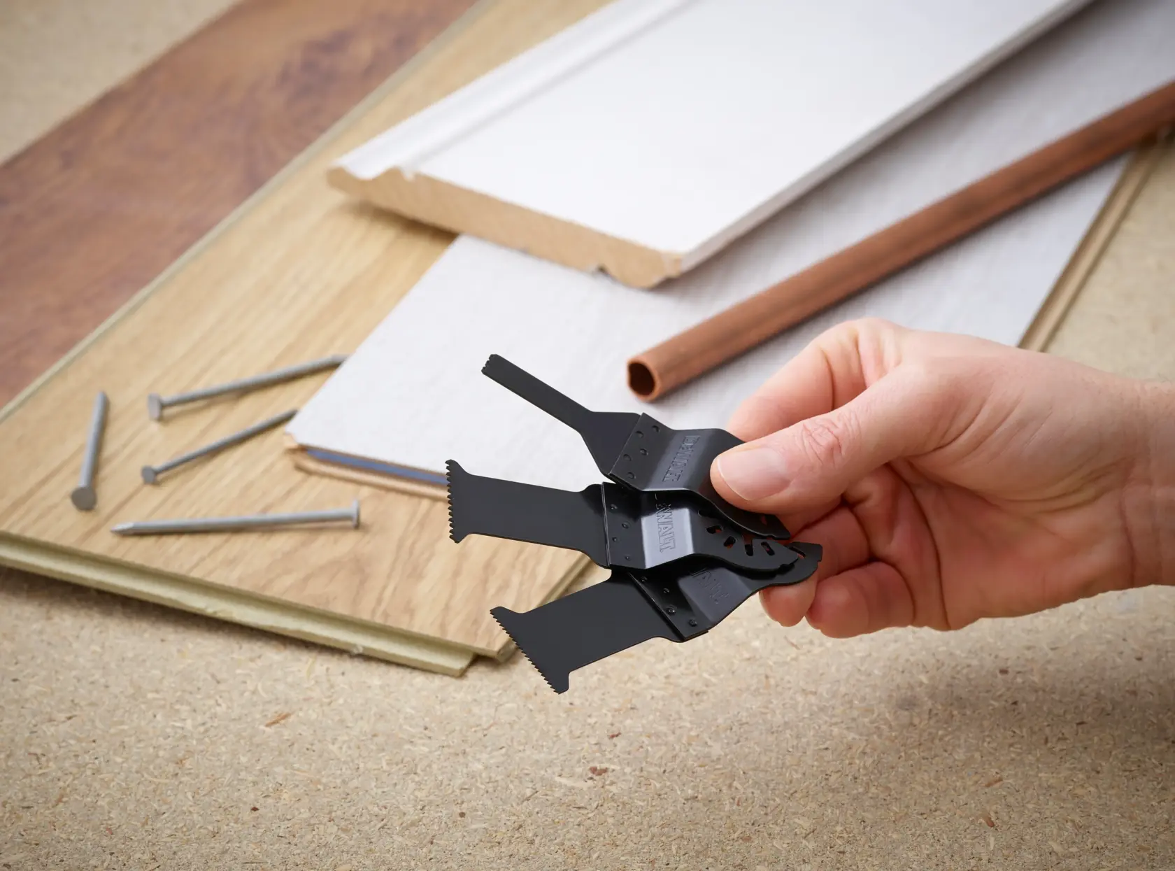 Hand hält DEWALT Multitool-Klingen, Nägel, Bretter und Rohr auf einer Werkbank.