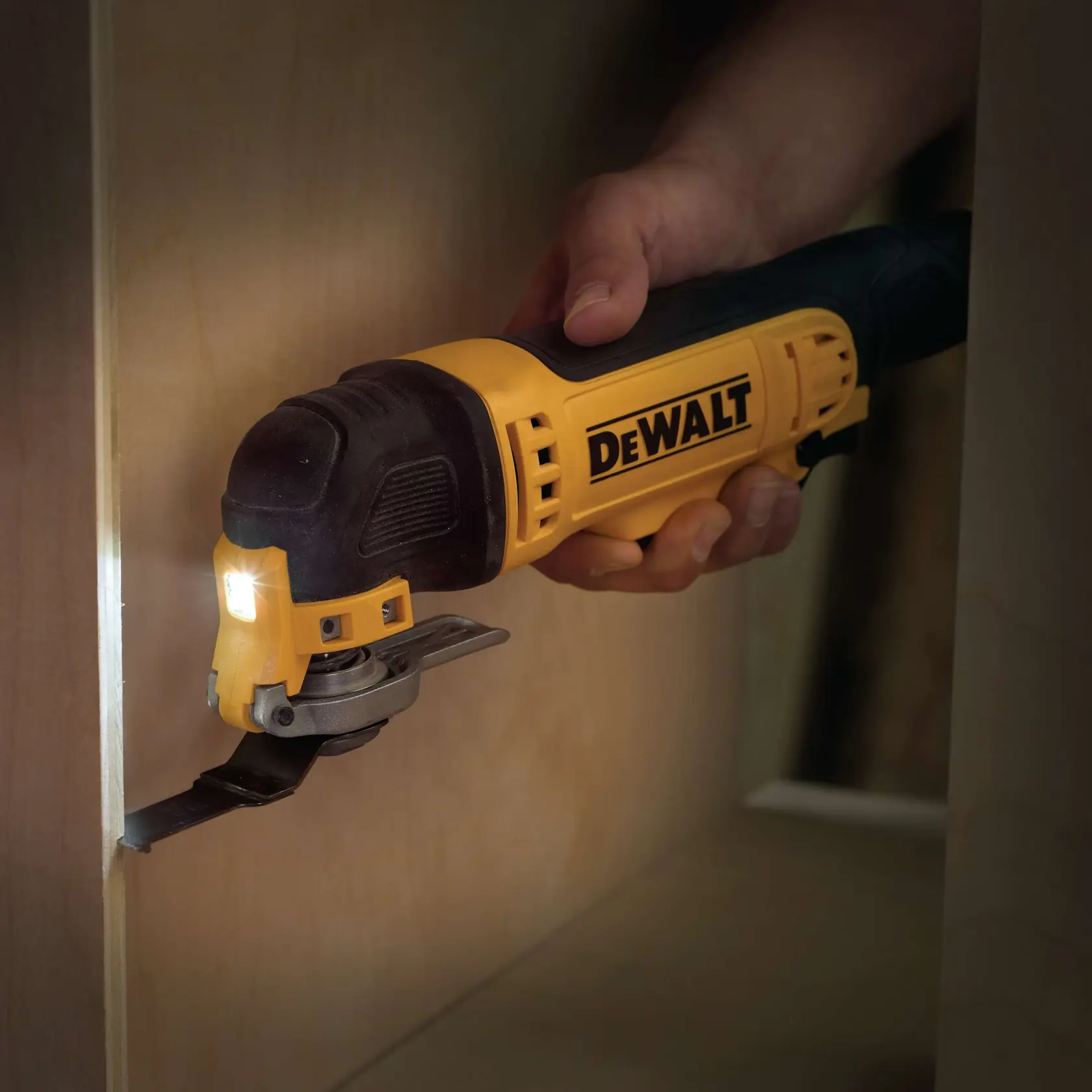Hand hält DEWALT-Oszillierwerkzeug mit LED, schneidet Holz in engem Bereich.