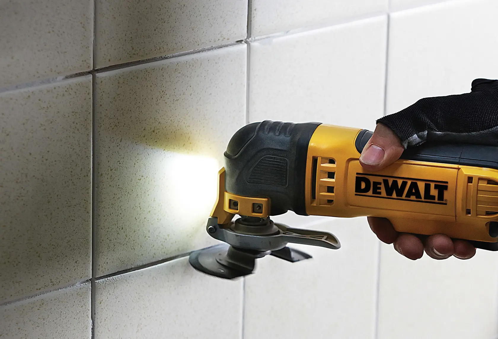 DEWALT multitool being used to cut tiles on a wall, close-up view of hand and tool in action.