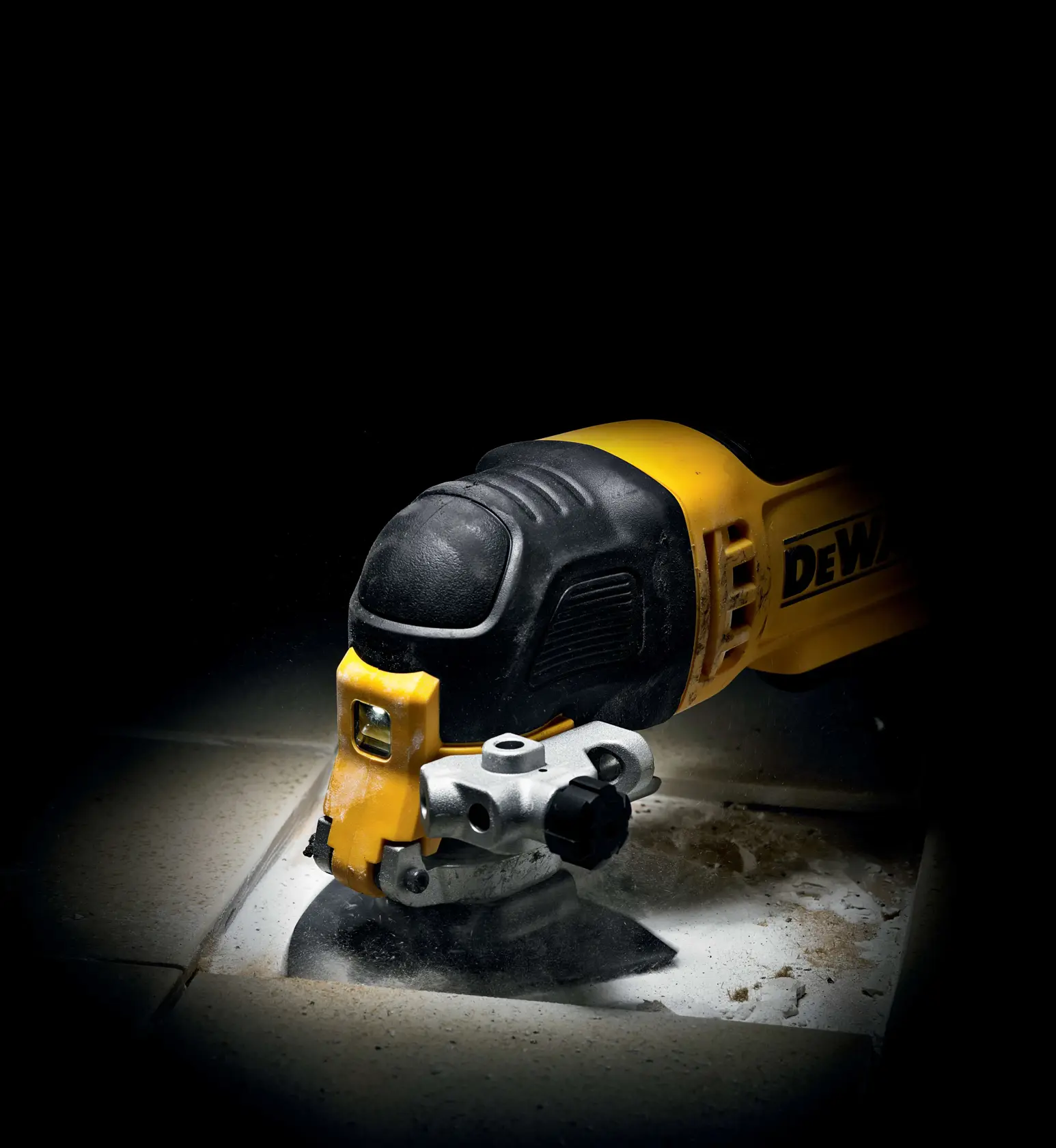 Multiherramienta DEWALT cortando azulejo, con polvo y escombros sobre la superficie.