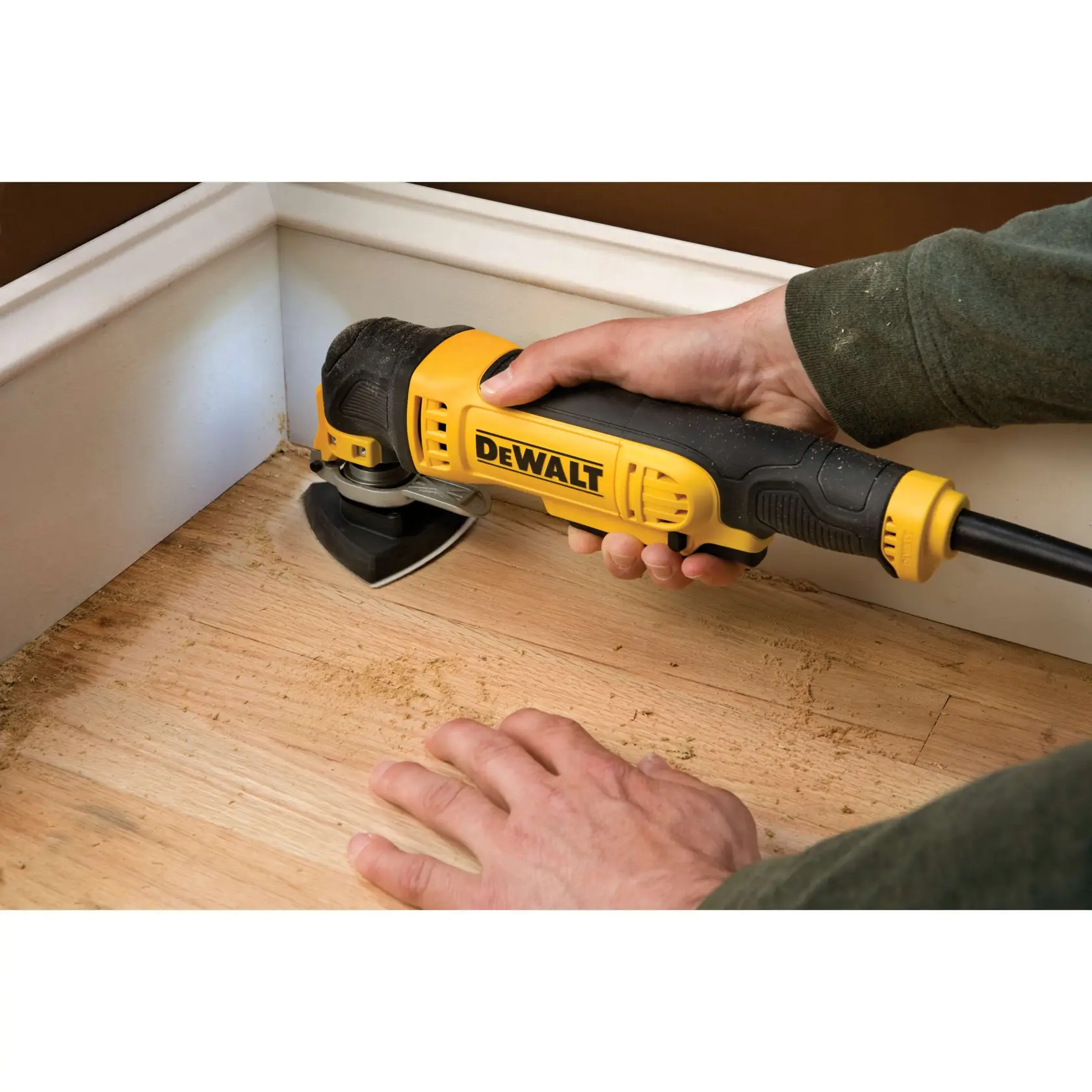 Herramienta DEWALT DT3092 lijando suelo de madera cerca del rodapié, sostenida por una persona.