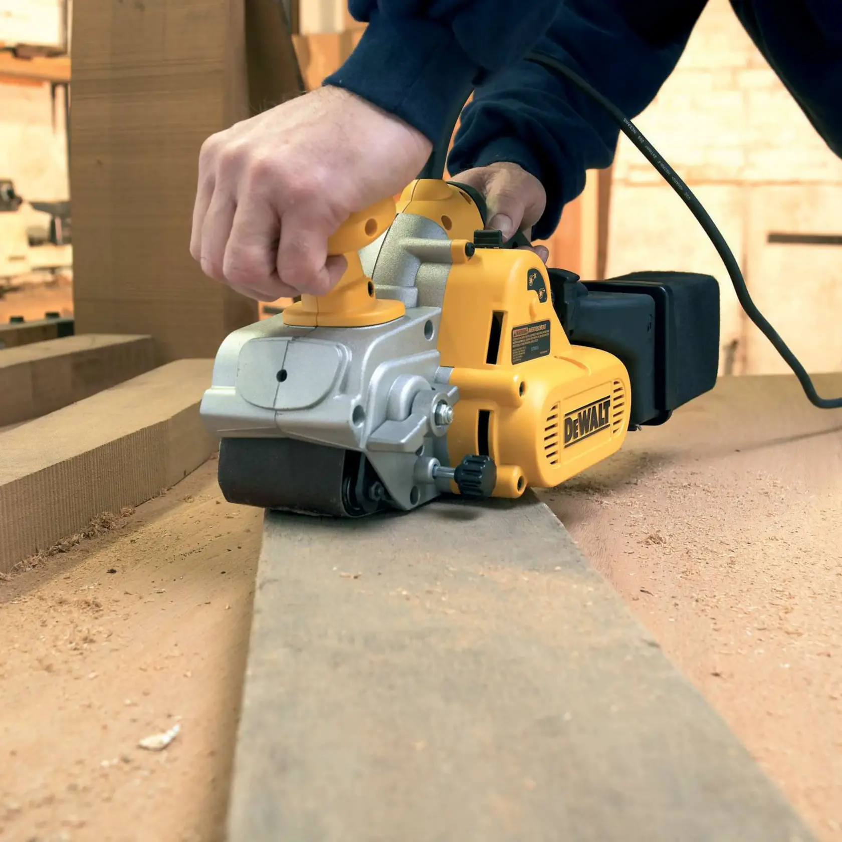 Lijadora de banda DEWALT en uso, lijando una tabla de madera con aserrín visible.