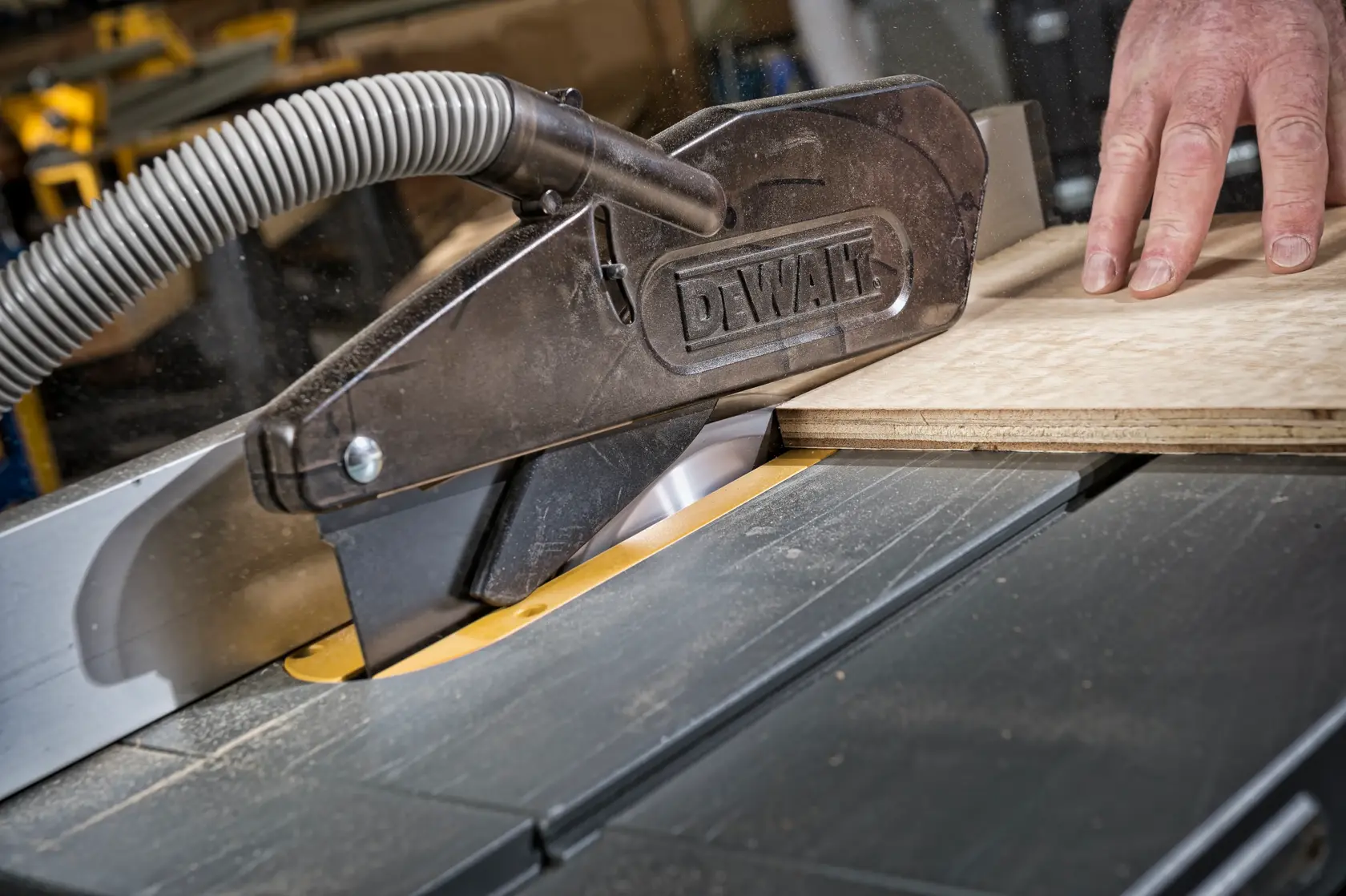DEWALT Säge schneidet Holz, Staubabsaugung und Hand auf Platte sichtbar.
