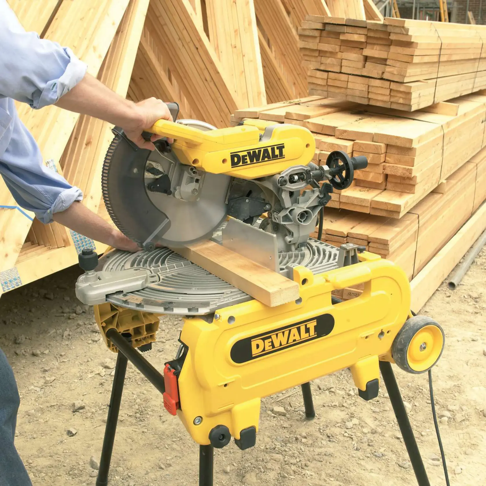 Sierra de inglete DEWALT cortando una tabla de madera en obra, con pilas de madera al fondo.