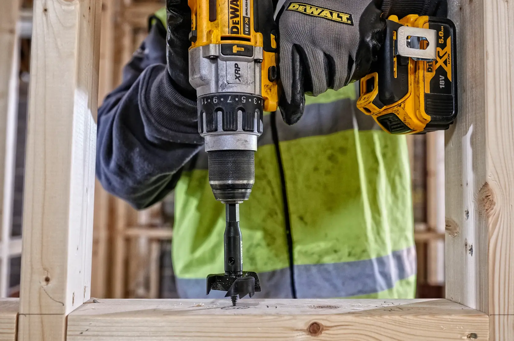 Persona usa taladro DEWALT en madera en obra, con guantes y chaqueta de seguridad.