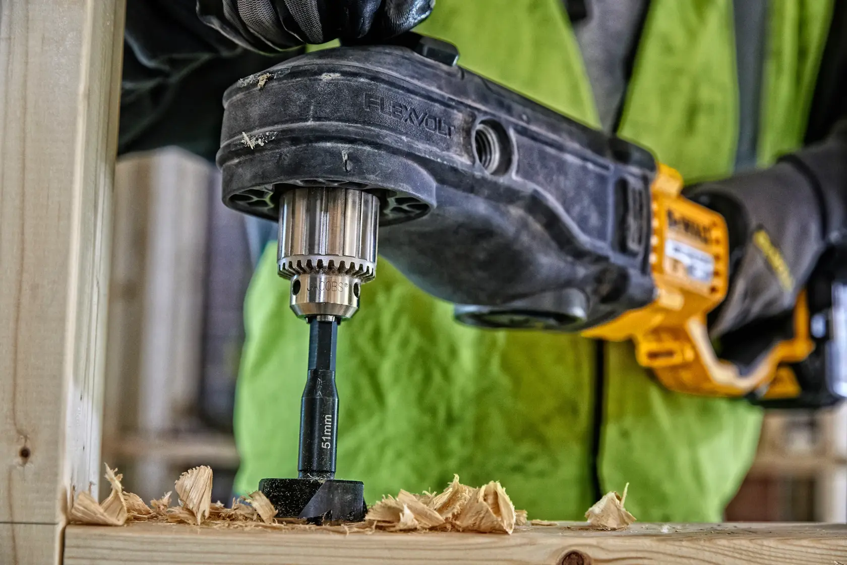 Taladro inalámbrico DEWALT perfora madera, trabajador con guantes en entorno de construcción.