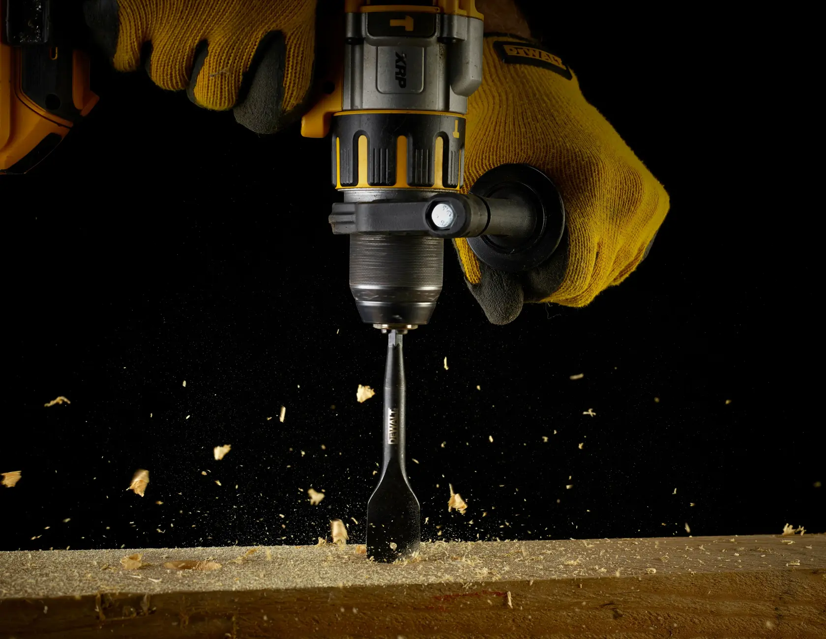 DEWALT drill with DT4768 spade bit drilling into wood, worn by gloved hands with wood shavings flying.