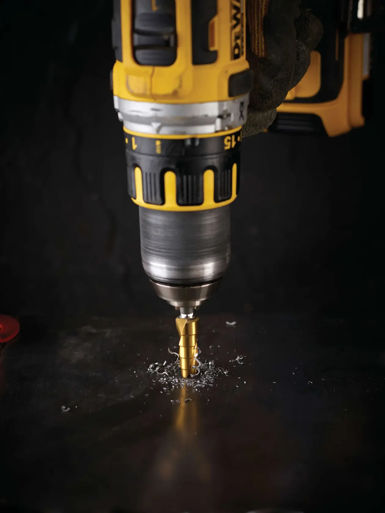 Taladro DEWALT con broca escalonada perforando metal y virutas metálicas alrededor de la broca.