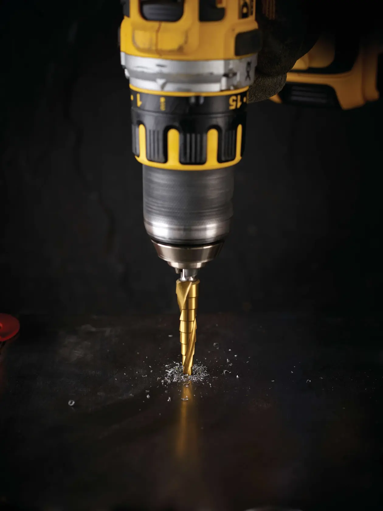 Taladro DEWALT con broca escalonada perfora una superficie metálica oscura y genera virutas.