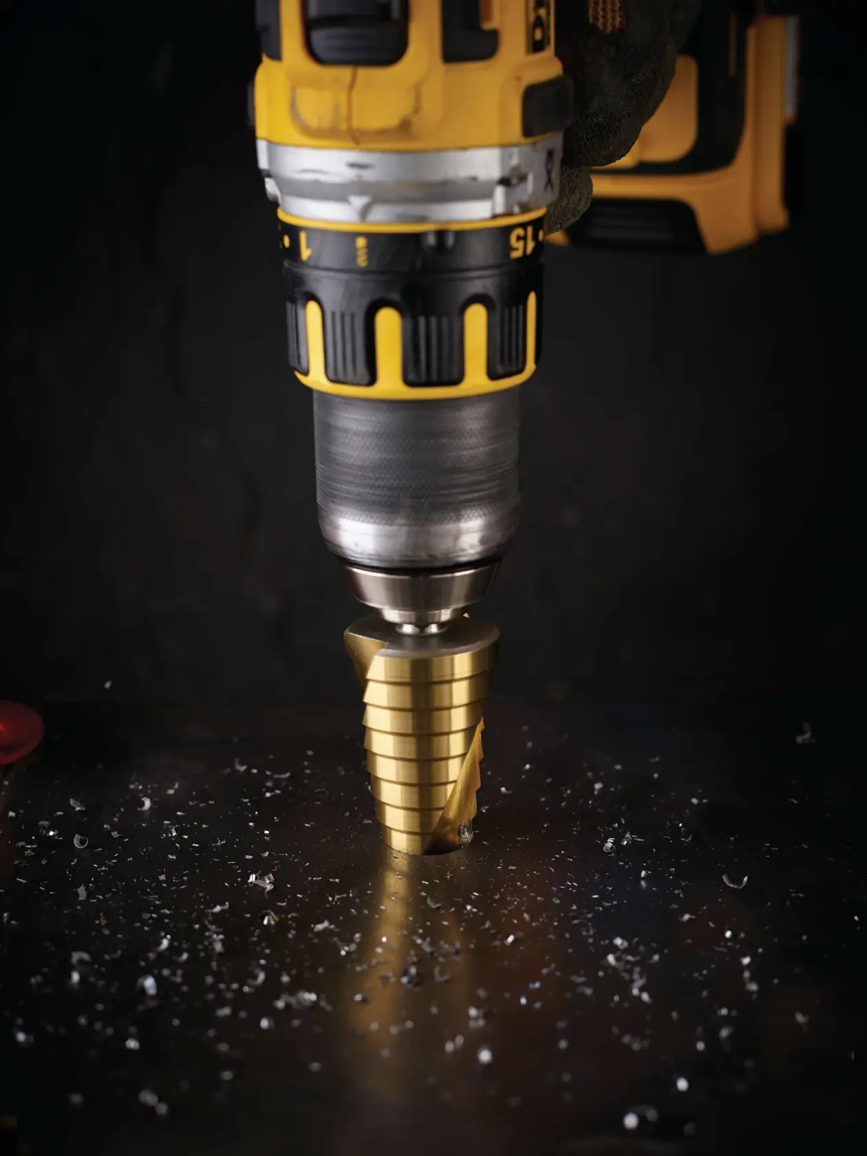 Close-up of a DEWALT drill with step drill bit cutting through a metal surface, surrounded by metal shavings.