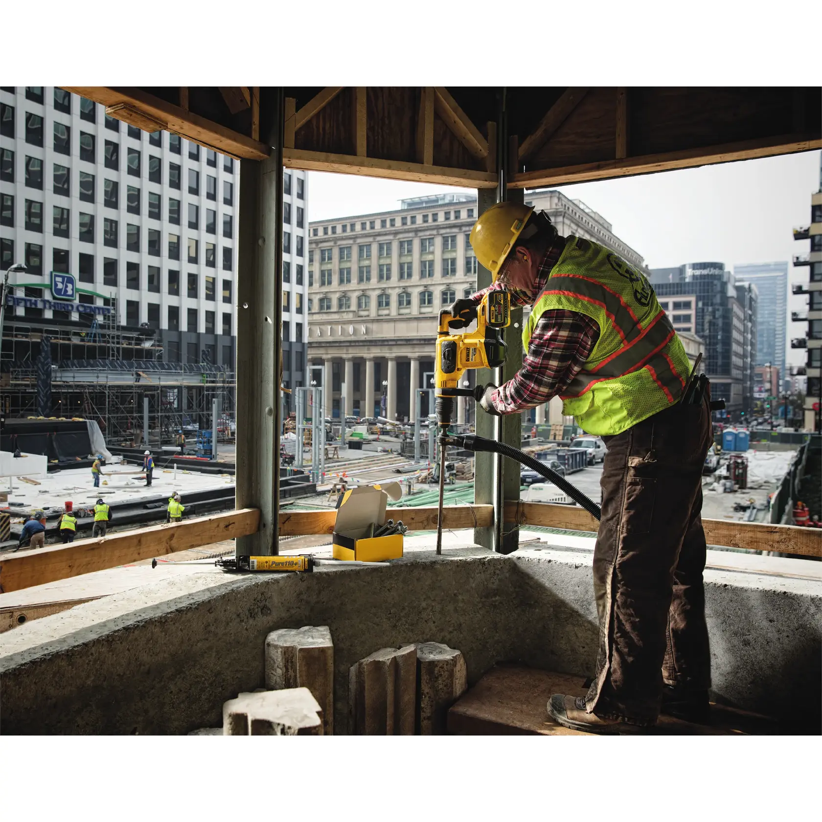 Trabajador usa taladro DEWALT en obra urbana, con chaleco y casco de seguridad.