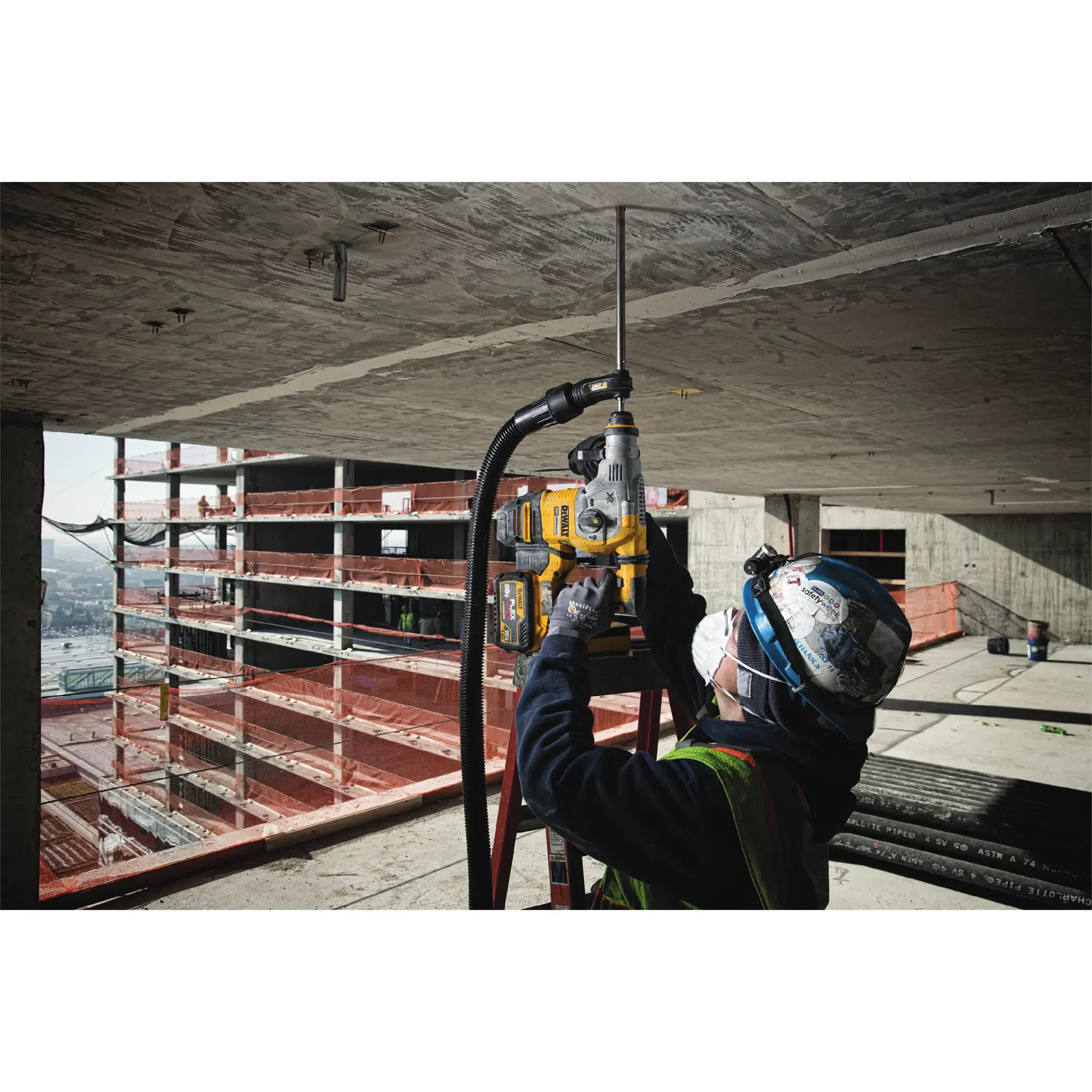 Trabajador usa taladro DEWALT con extractor de polvo para perforar techo de concreto en obra.