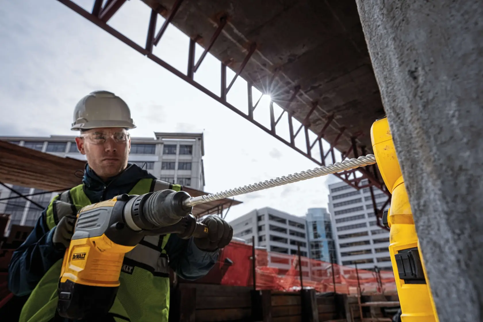 Trabajador usa taladro DEWALT con DT60817 en obra, perfora concreto cerca de edificios.
