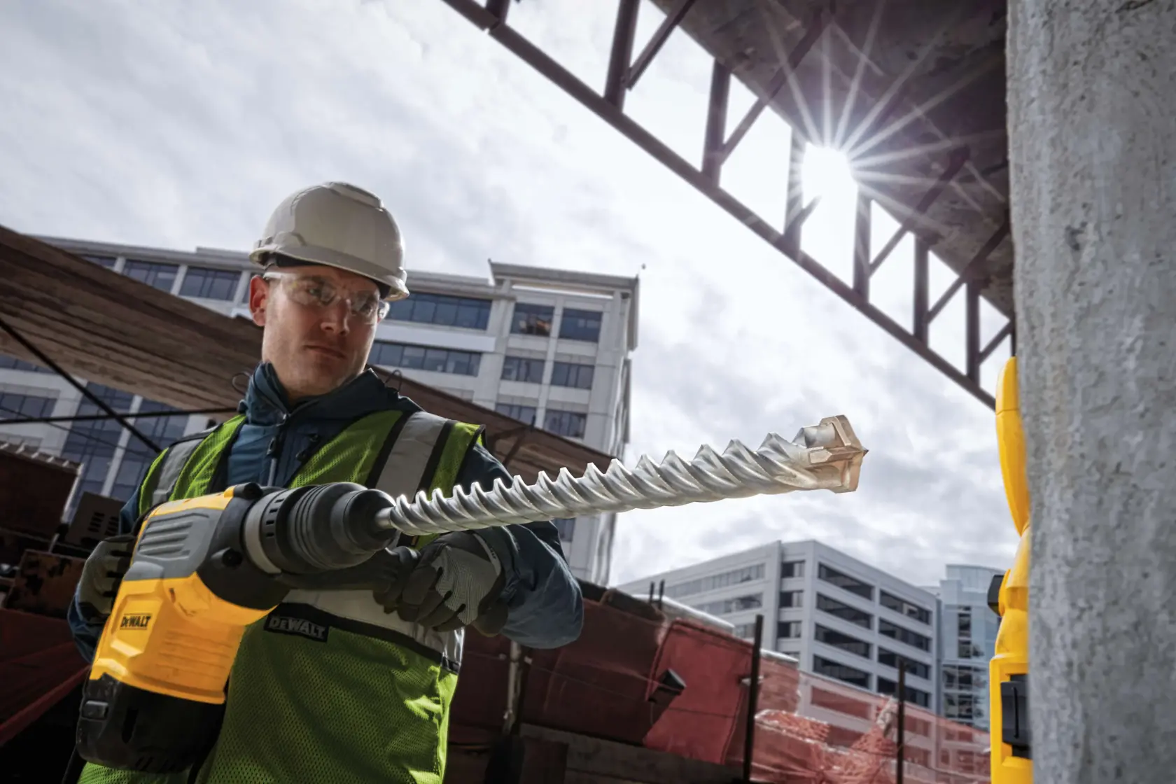 Broca DEWALT DT60835 utilizada en obra. Trabajador con equipo de seguridad cerca de edificios.