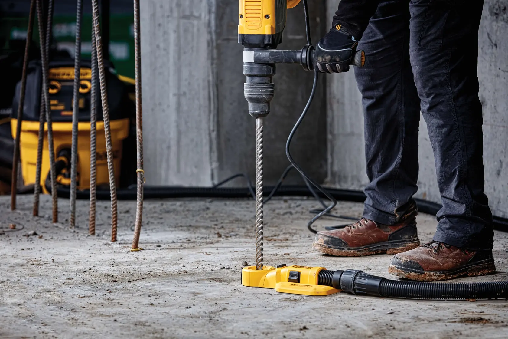 Trabajador usa taladro DEWALT sobre cemento, con varillas y extracción de polvo en obra.