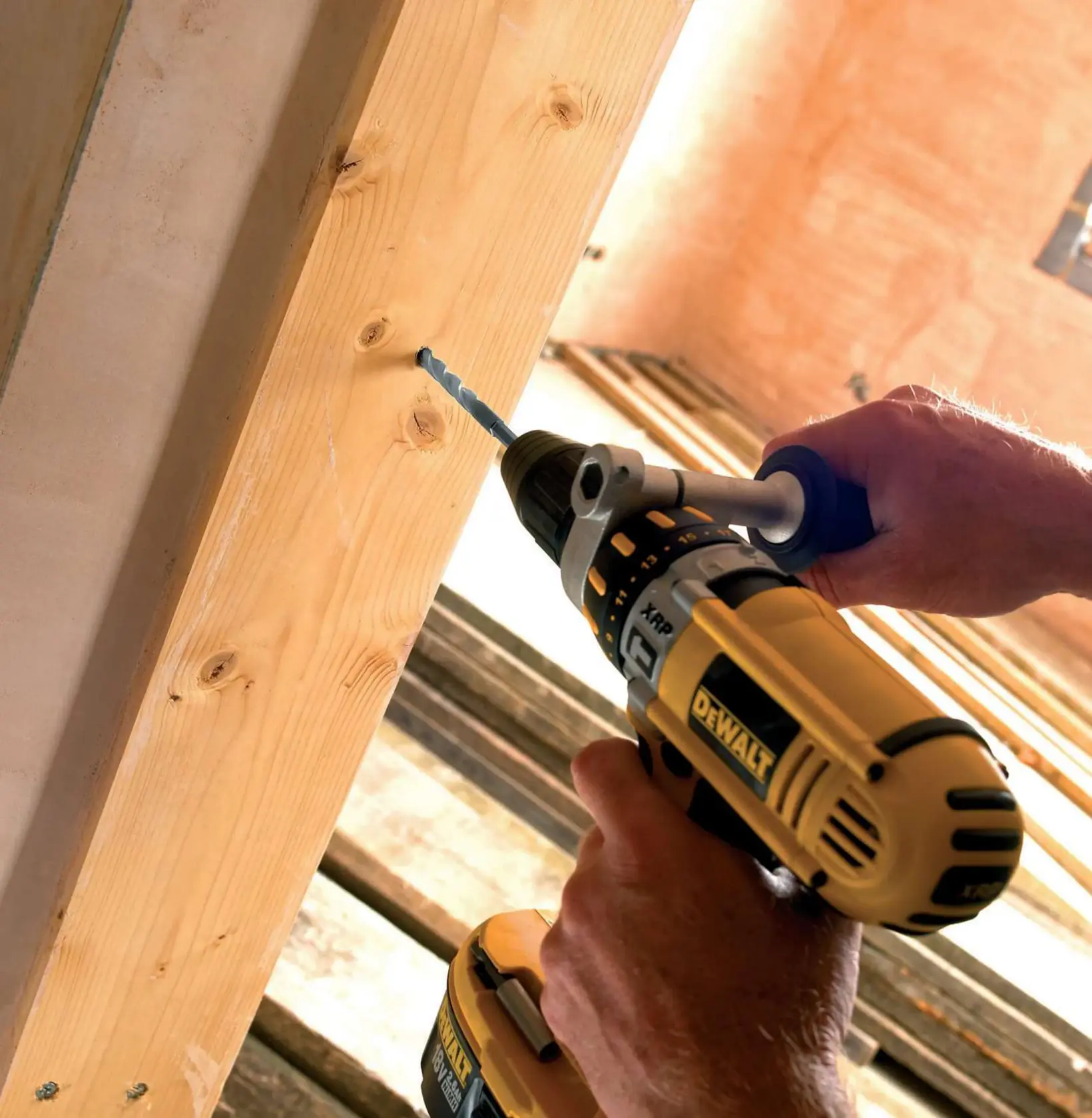 Persona usa un taladro DEWALT para hacer un agujero en una viga de madera.