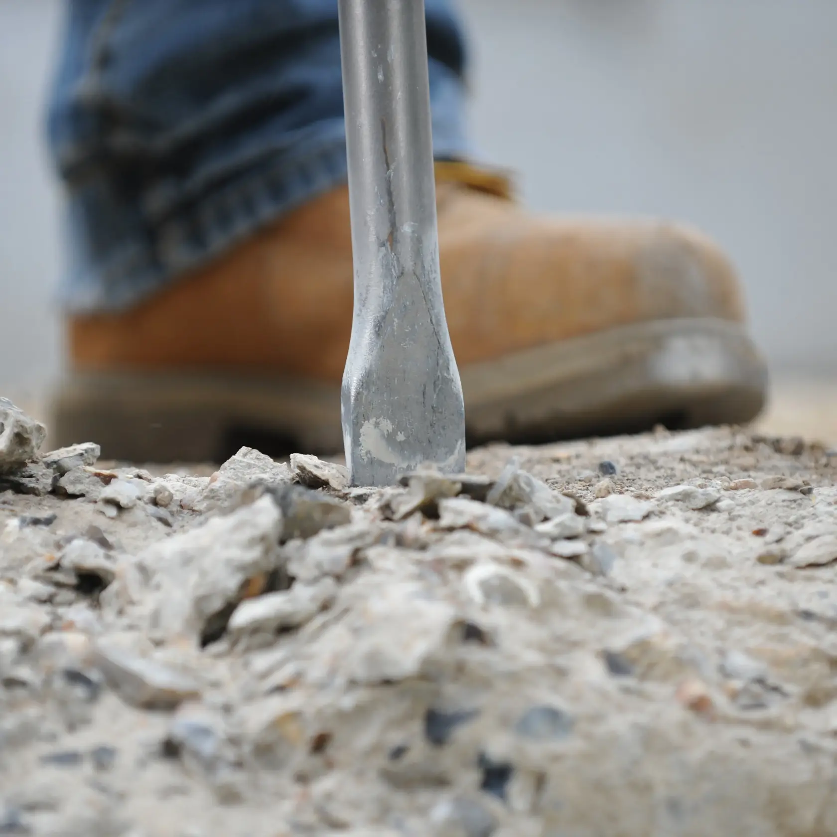 Close-up of a DEWALT chisel tool breaking concrete with a boot in the background.