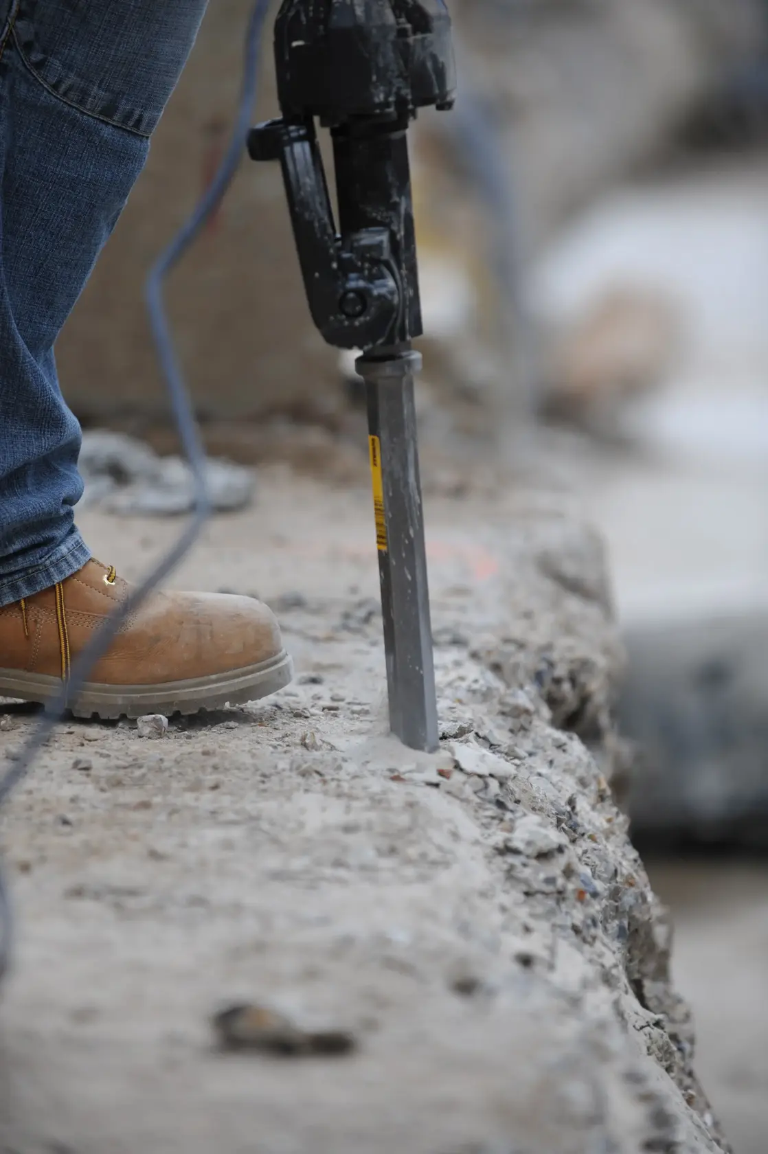 Worker uses a rotary hammer with a chisel bit drilling into concrete slab on a construction site.