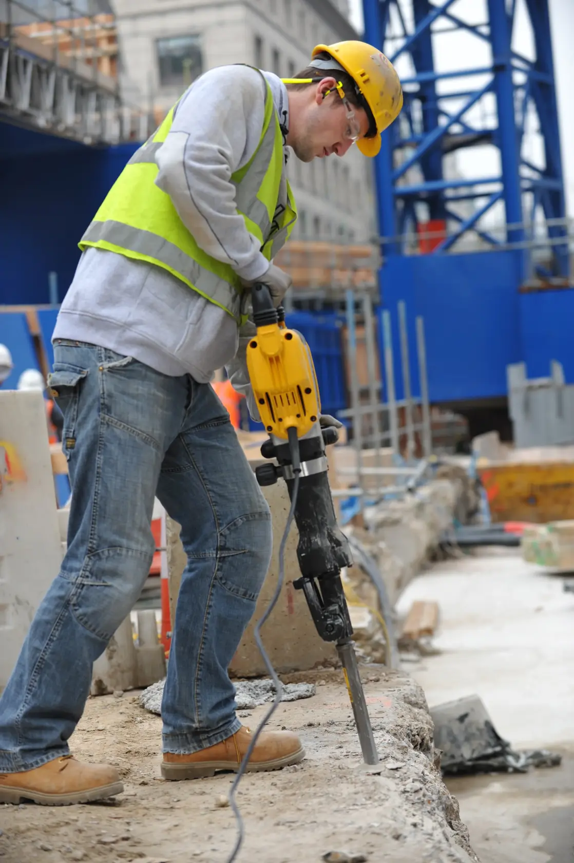 Worker using DEWALT jackhammer DT6927 on concrete at construction site, wearing safety gear and helmet.