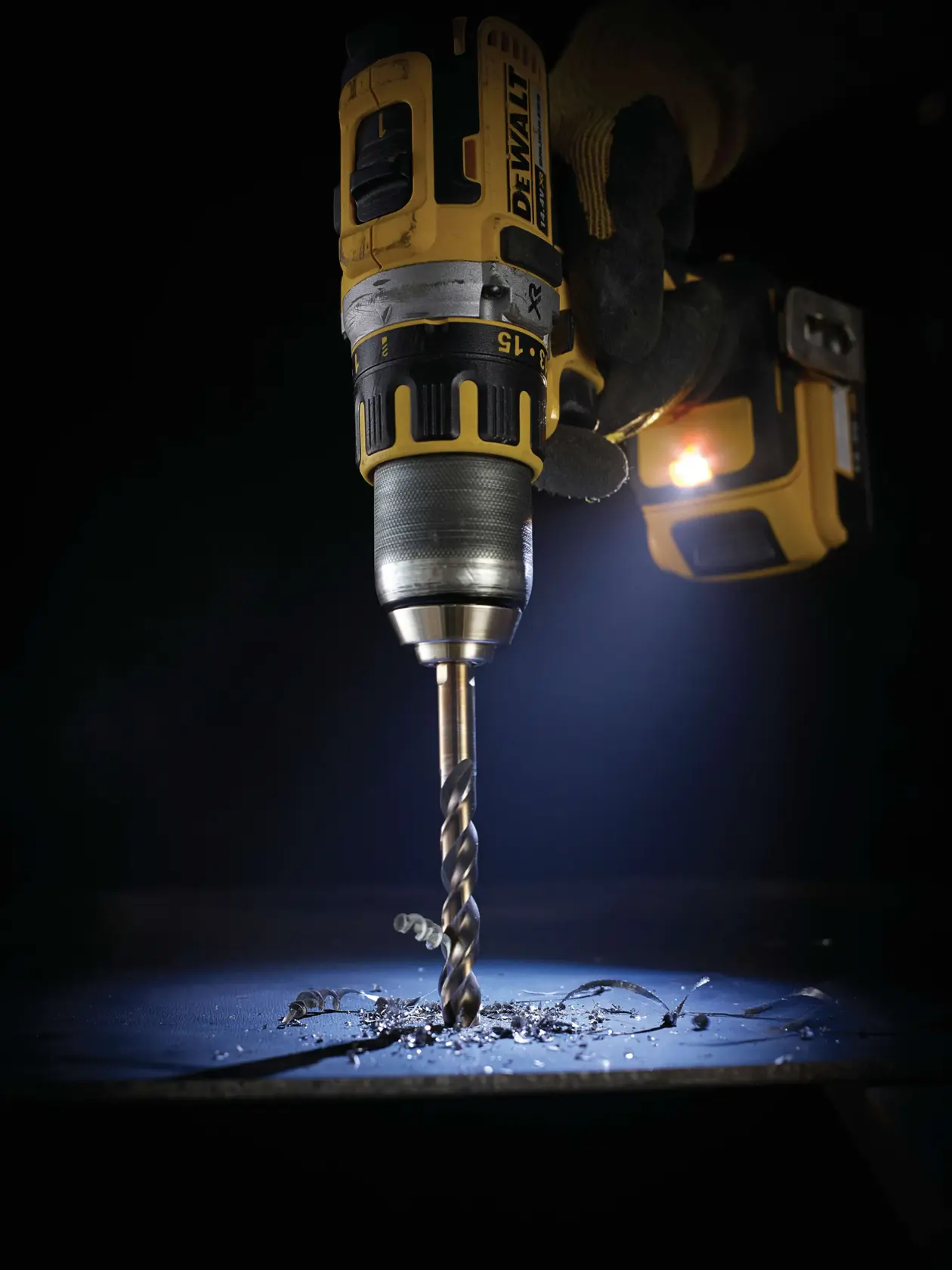 DEWALT cordless drill in use, drilling into metal with visible shavings and LED light illuminating the area.