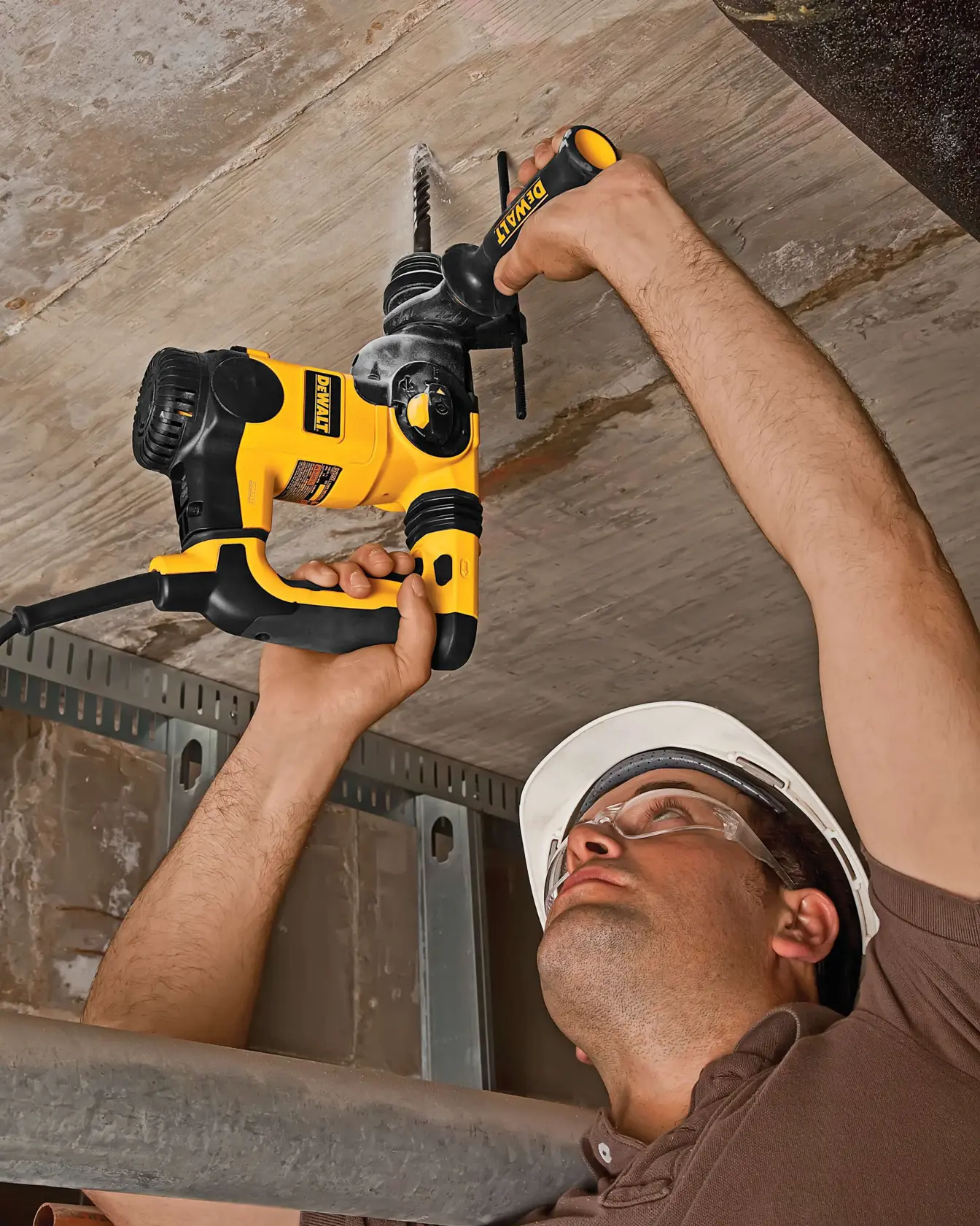 Persona usa martillo rotativo DEWALT en techo de concreto. Rostro borroso, herramienta destacada.