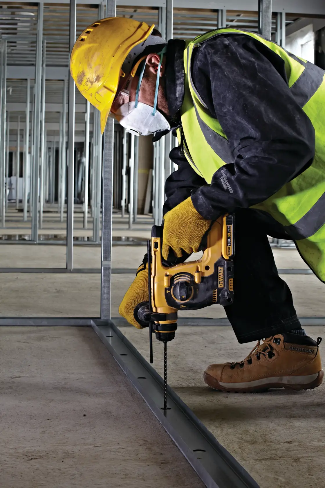 Trabajador con equipo de seguridad usa un taladro DEWALT en un armazón metálico en construcción.