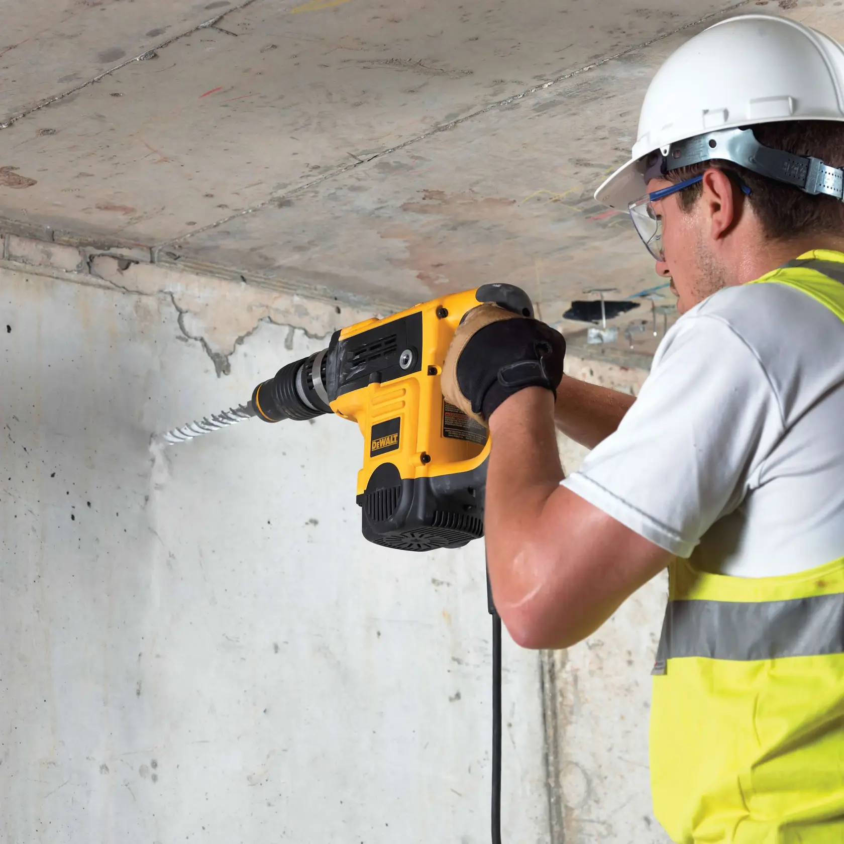 Person bohrt mit DEWALT DT9409 durch Betonwand, trägt Sicherheitsausrüstung und Handschuhe.