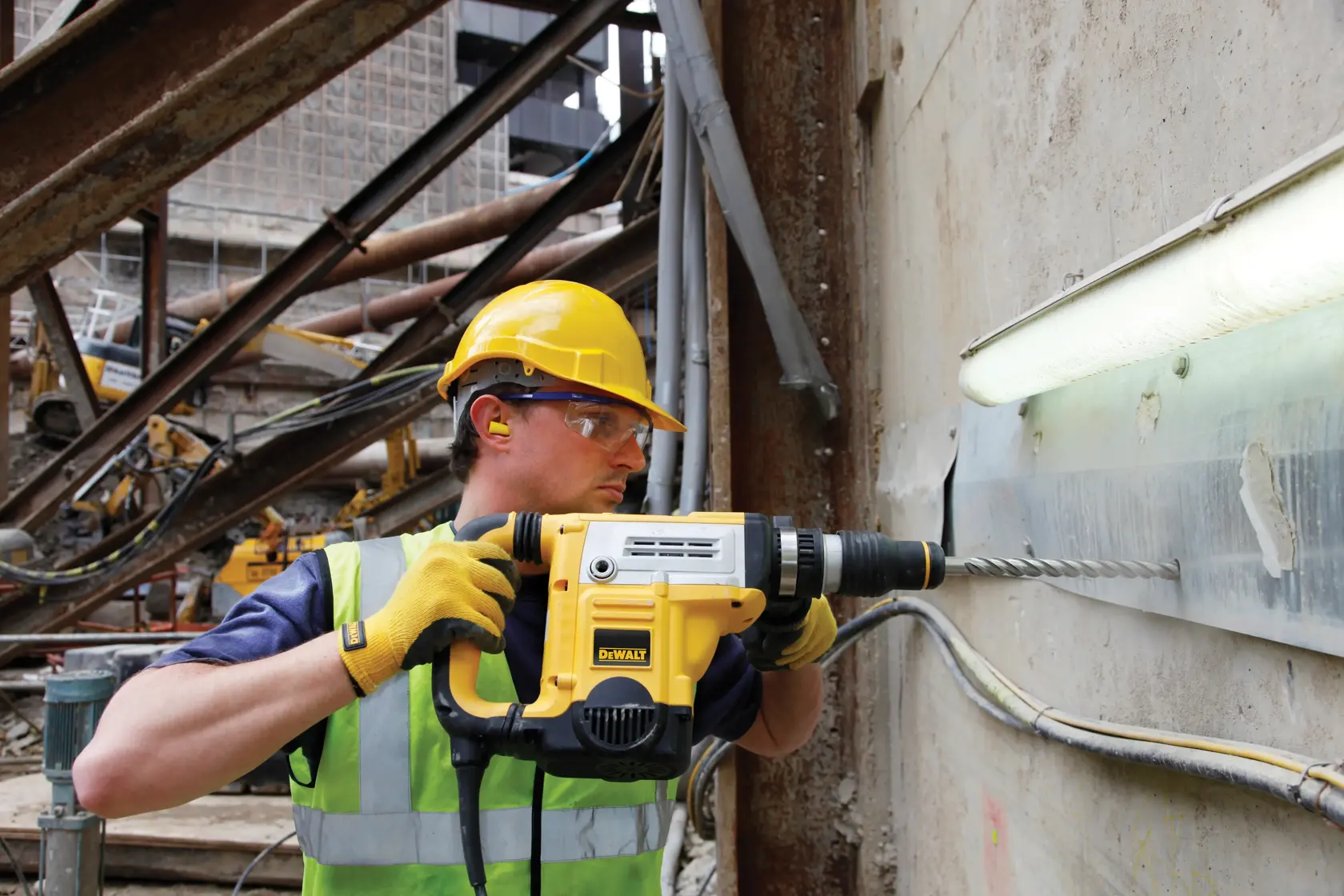 Arbeiter nutzt einen DEWALT Schlagbohrer an einer Betonwand auf einer Baustelle.