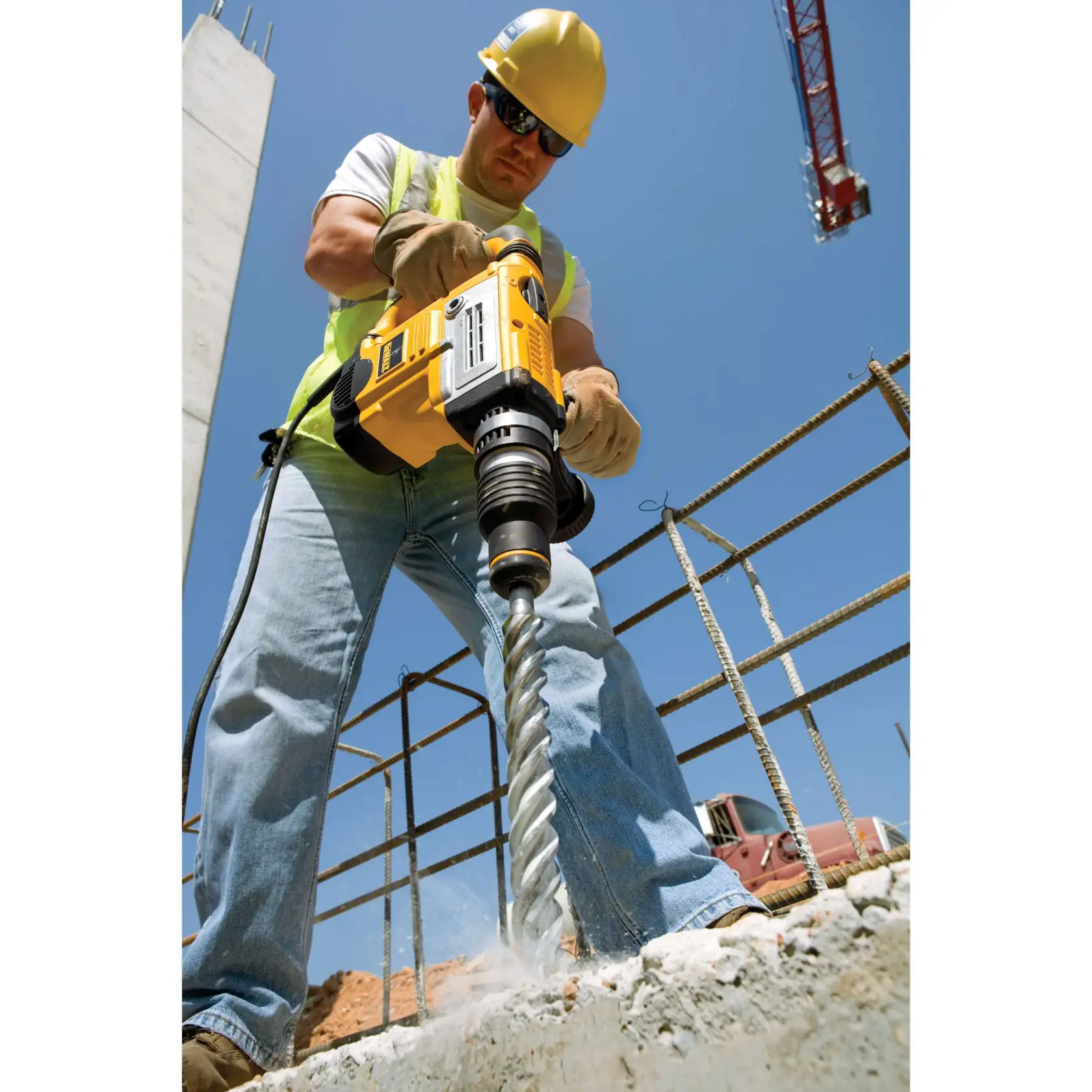 Person nutzt eine DEWALT-Bohrmaschine auf Beton an einer Baustelle bei Sonnenschein.