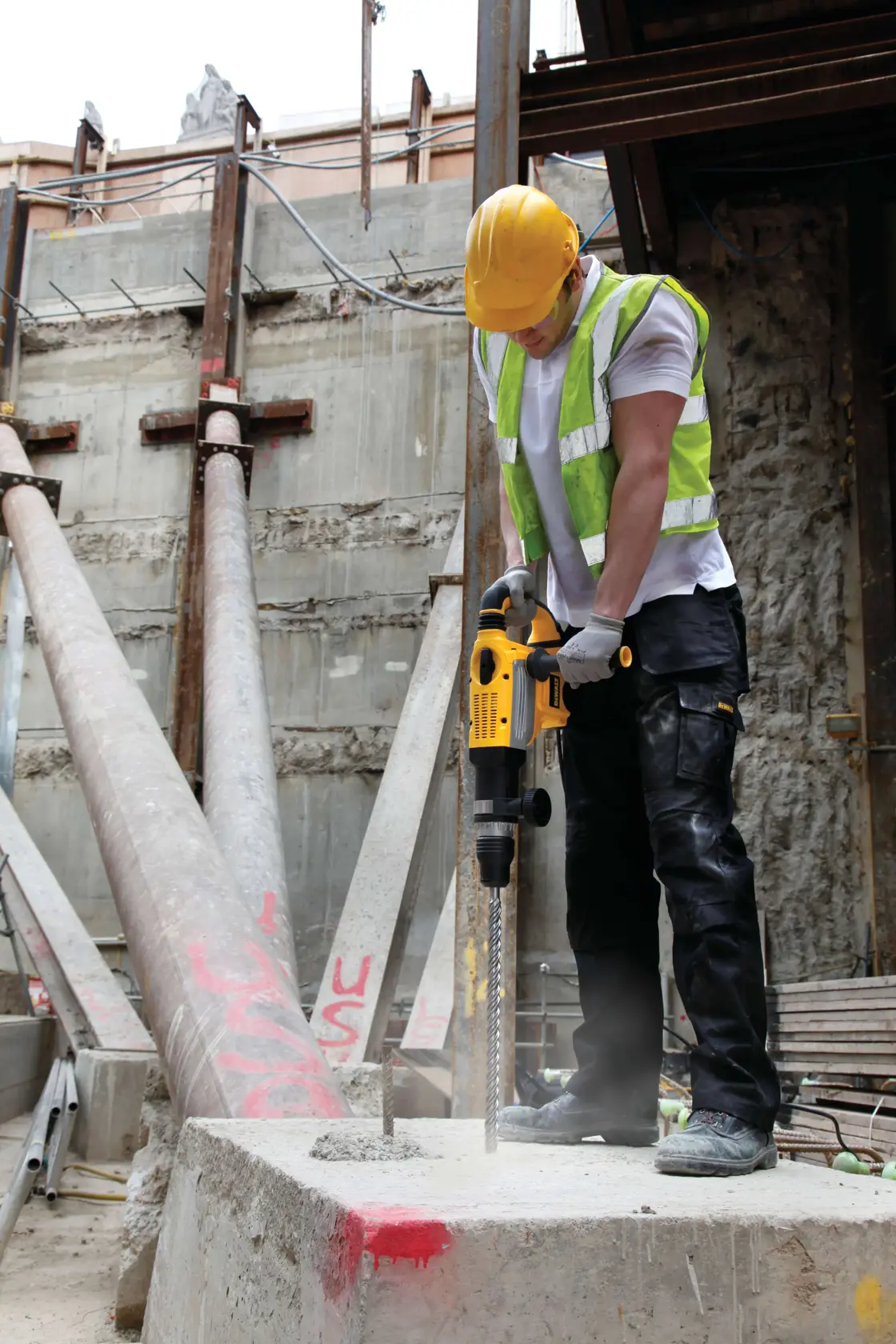 Arbeiter benutzt DEWALT Schlagbohrmaschine auf Baustelle zum Bohren in Beton, mit Schutzkleidung.
