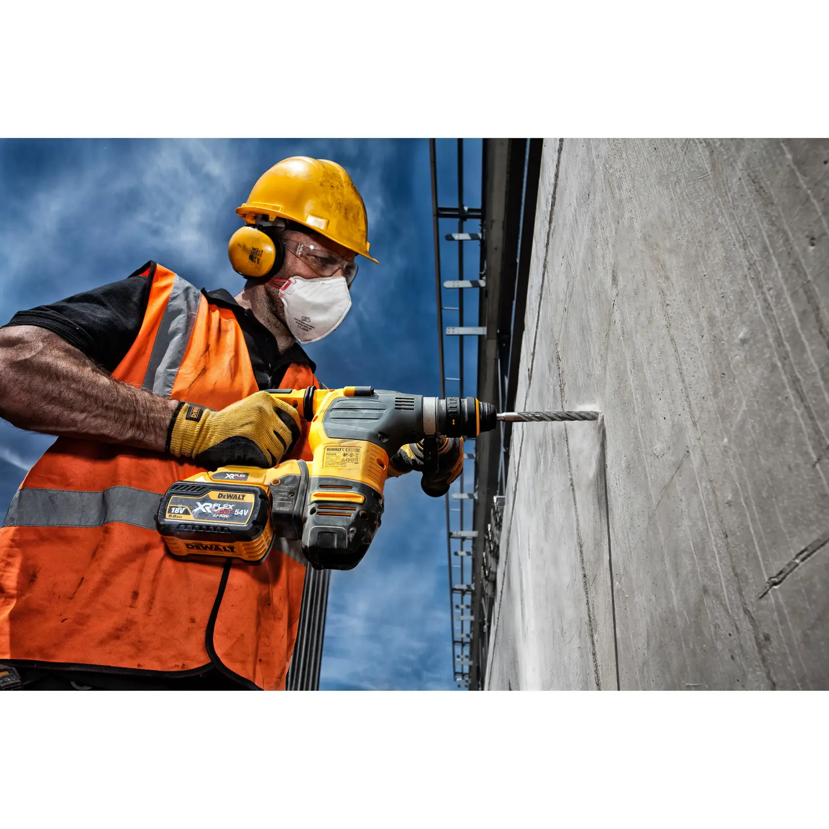 Trabajador con equipo de seguridad perfora pared de concreto con taladro inalámbrico DEWALT al aire libre.
