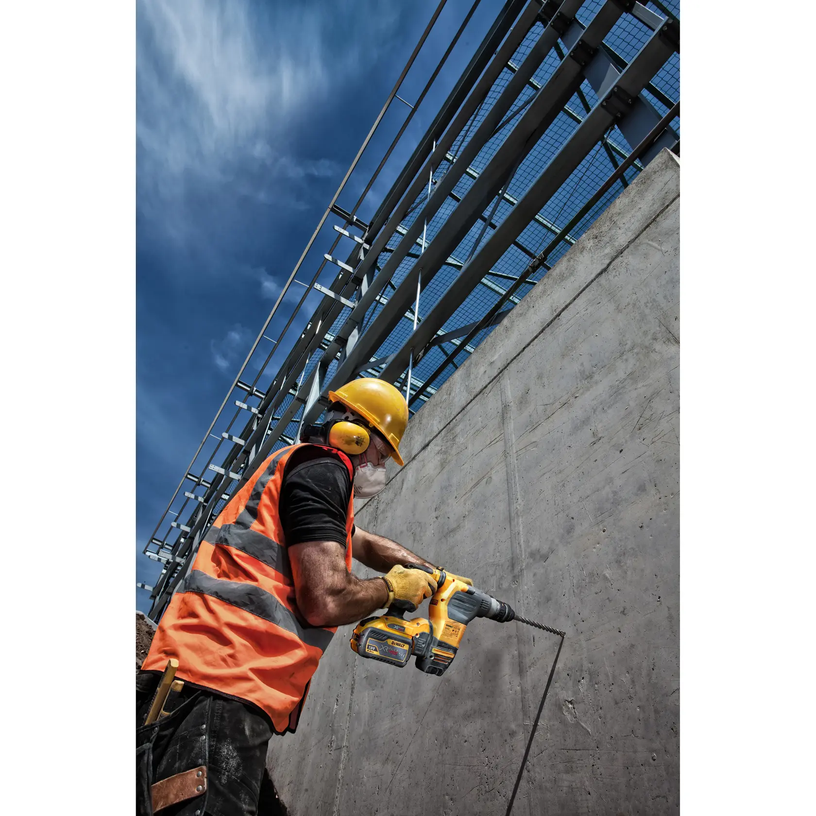 Trabajador con equipo de seguridad usa un taladro DEWALT en una pared de concreto en la obra.