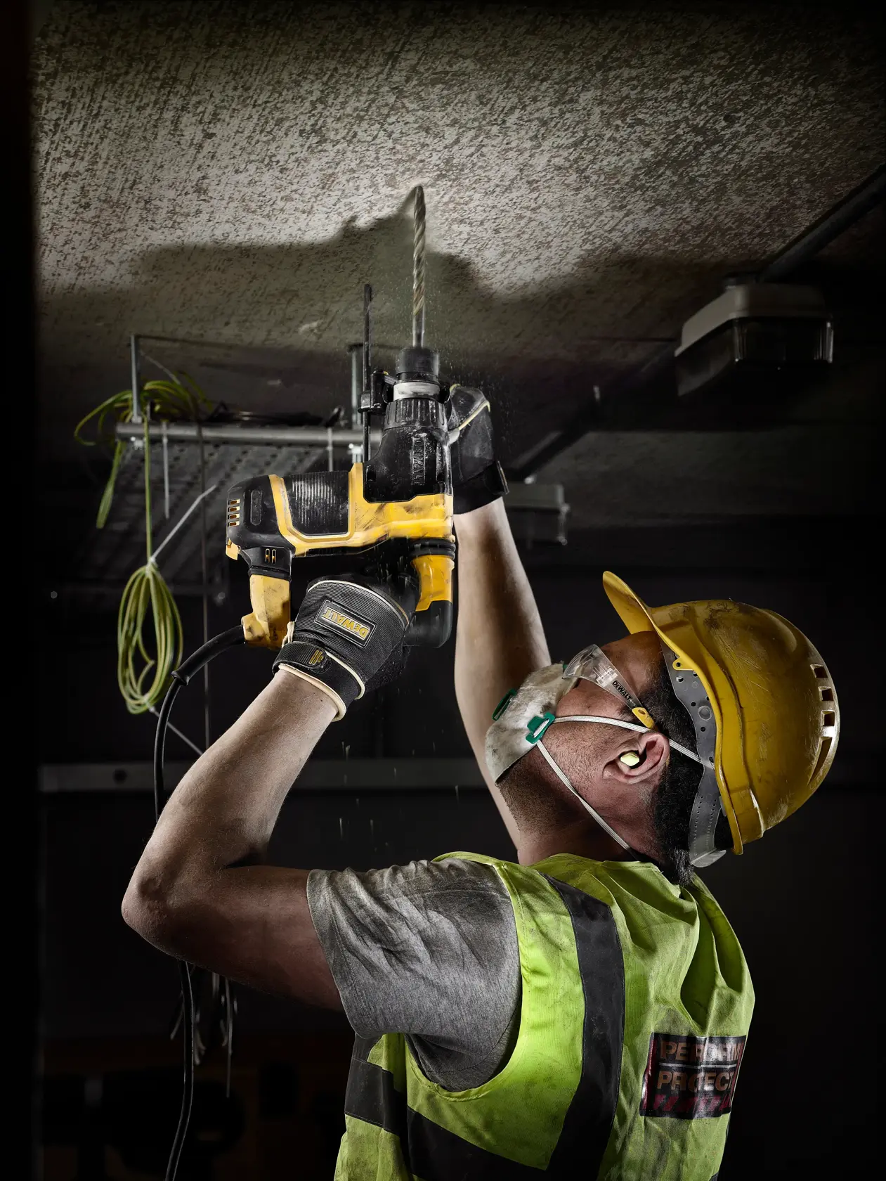 Trabajador usa taladro DEWALT DT9625 en techo, con casco, guantes, chaleco, mascarilla y protección auditiva.